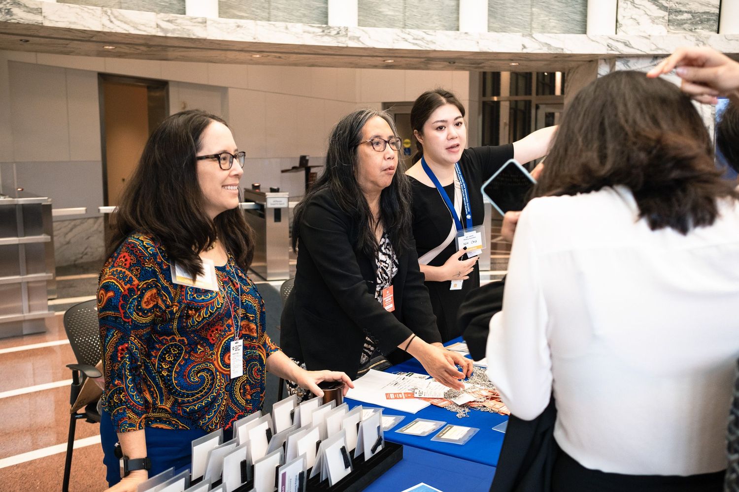 Women networking at a professional conference registration table in a modern building.