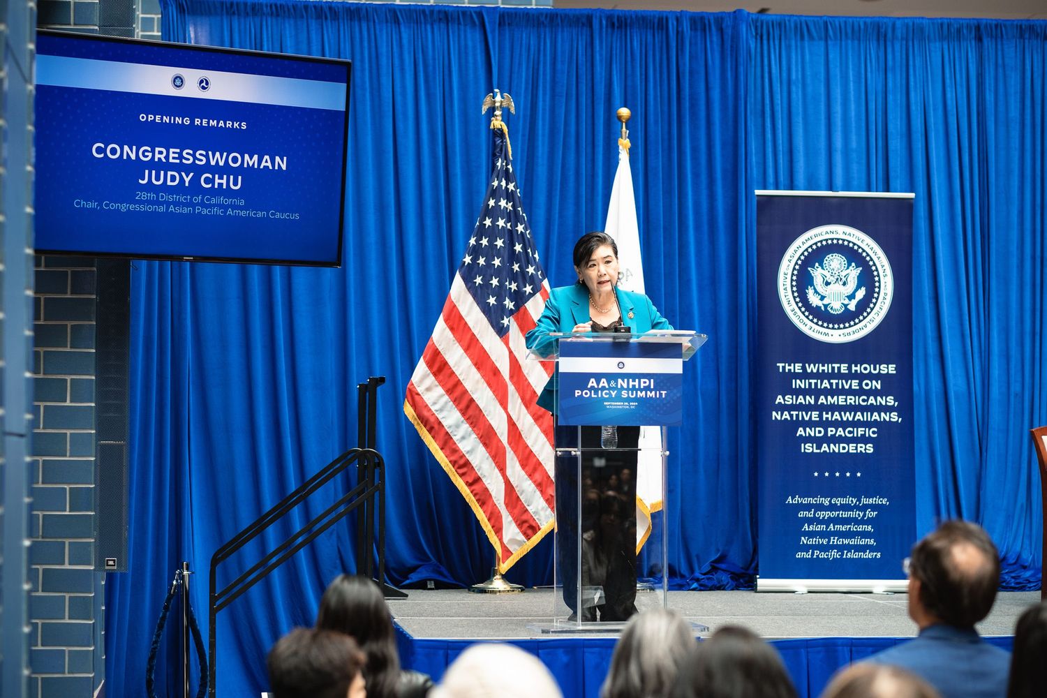Congresswoman Judy Chu speaks at the White House Initiative AA & NHPI Policy Summit podium with American flag.