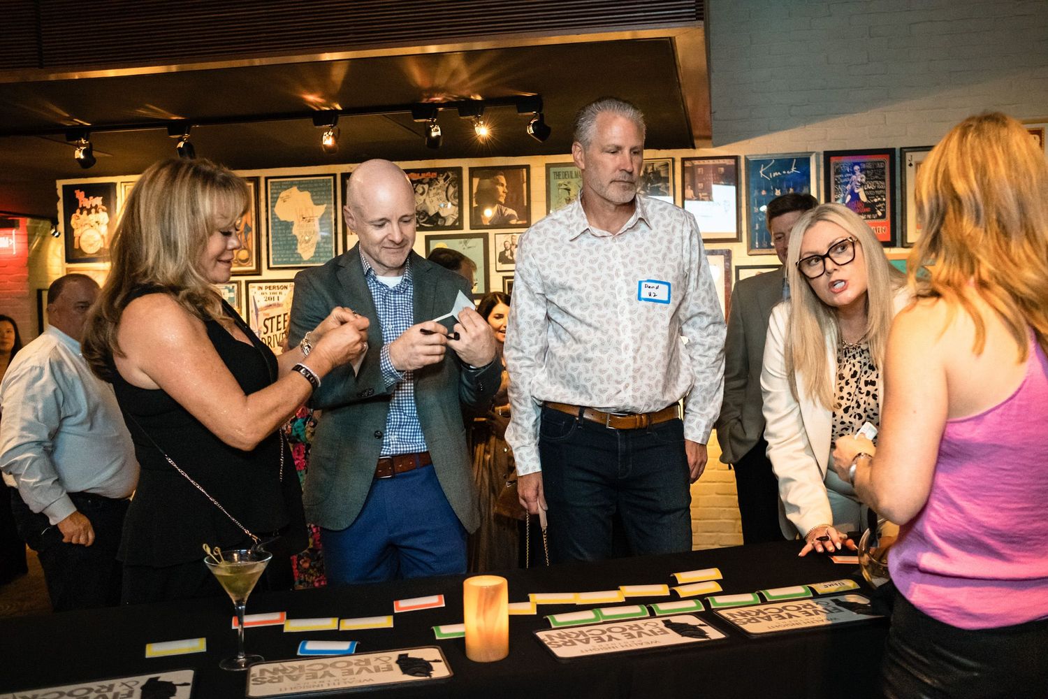 Group of people gathered around a table at an indoor networking event, examining items on display in a gallery setting.
