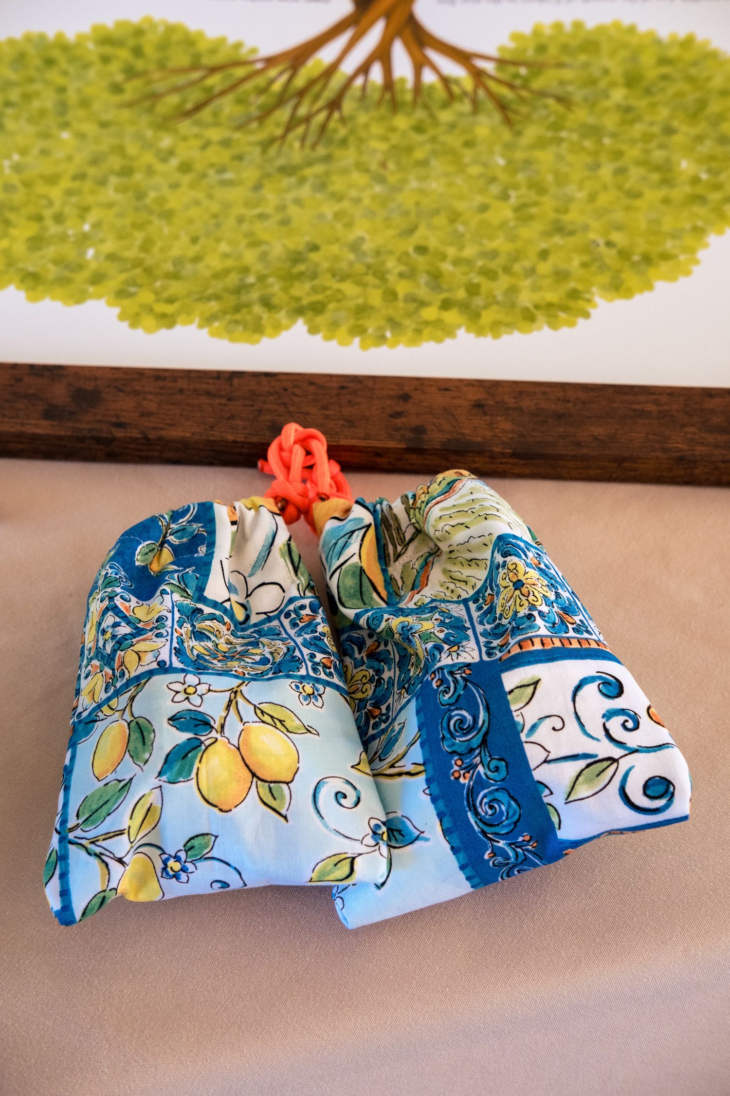 Colorful blue floral fabric pouch with lemon print tied with an orange bow displayed on a wooden shelf.