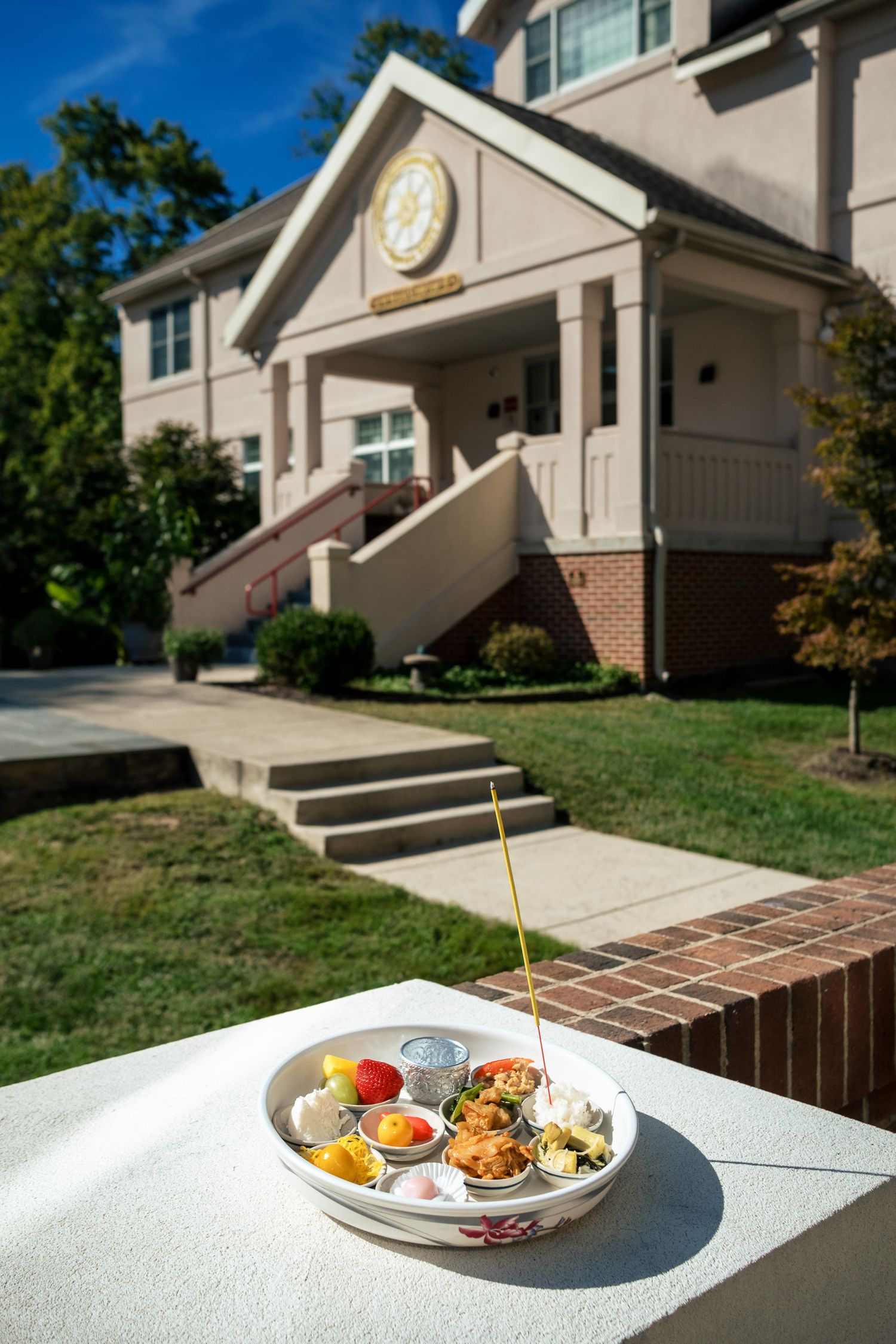 Traditional Thai offering plate with incense sticks displayed outdoors in front of a beige ceremonial building.