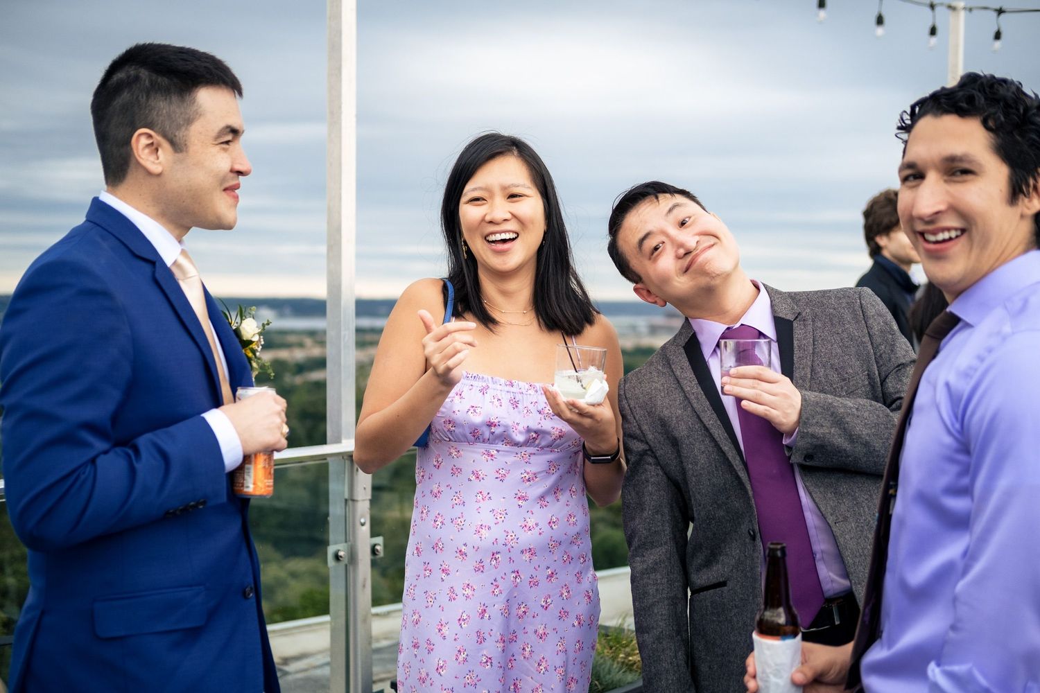Four guests laugh and chat together on a rooftop terrace during a wedding cocktail hour.