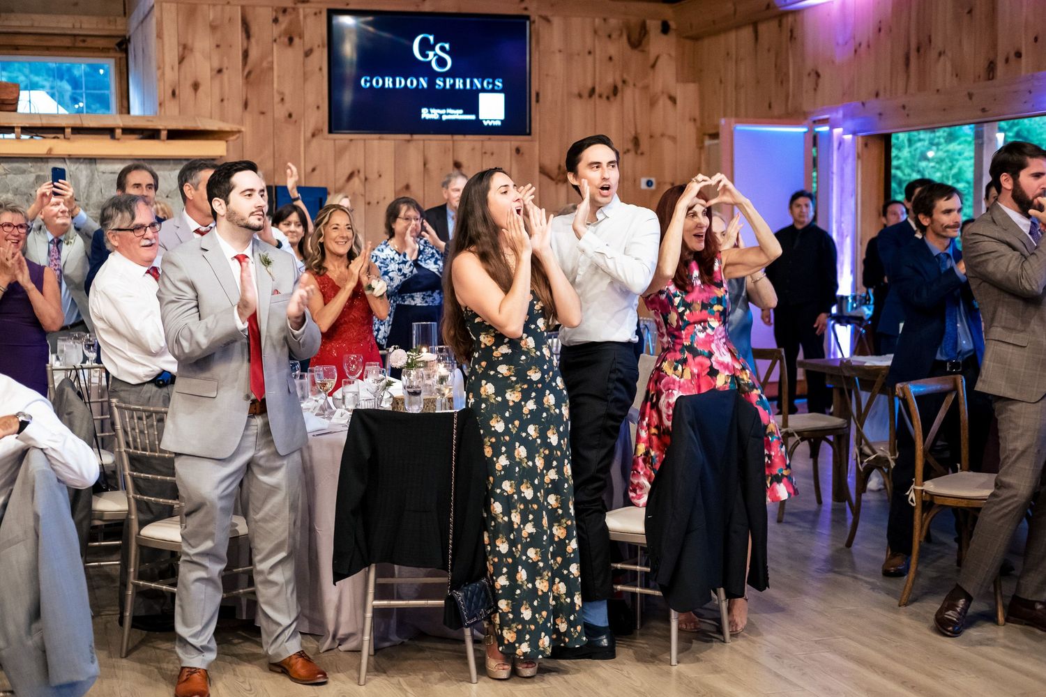 Joyful wedding guests clap and make heart gestures during reception at Gordon Springs barn venue.