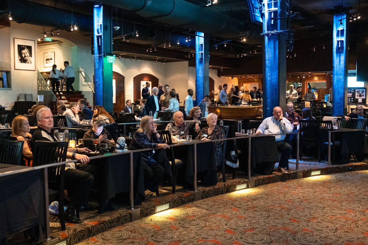 Guests seated in a stylish venue with blue lighting, enjoying an evening event in an upscale entertainment space.