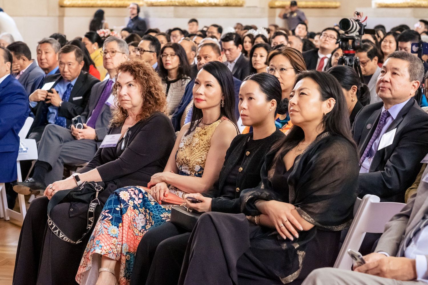 Diverse audience seated at a formal conference event, attentively listening to speakers in an elegant venue.