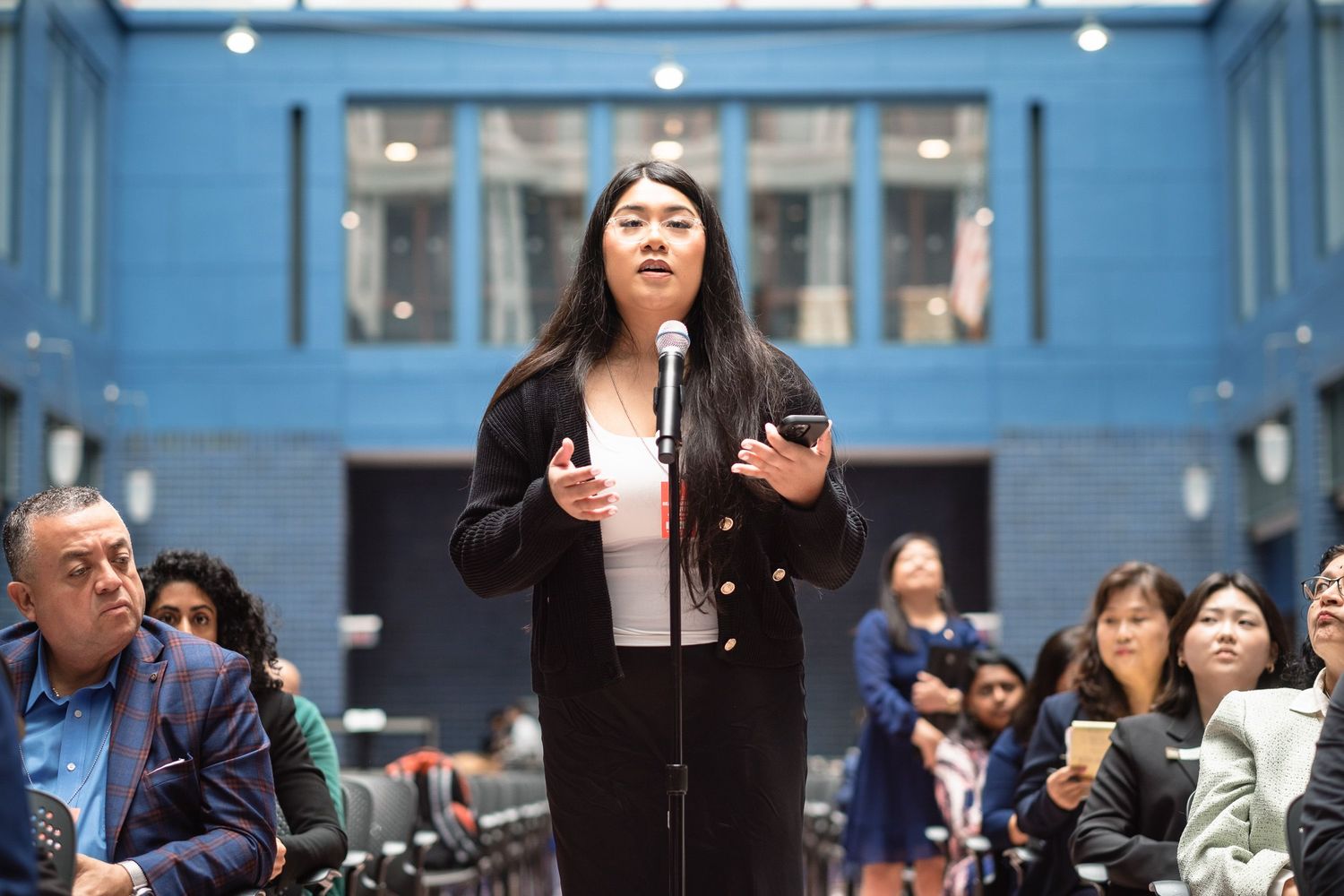 Young woman speaking at microphone during audience Q&A at policy conference.