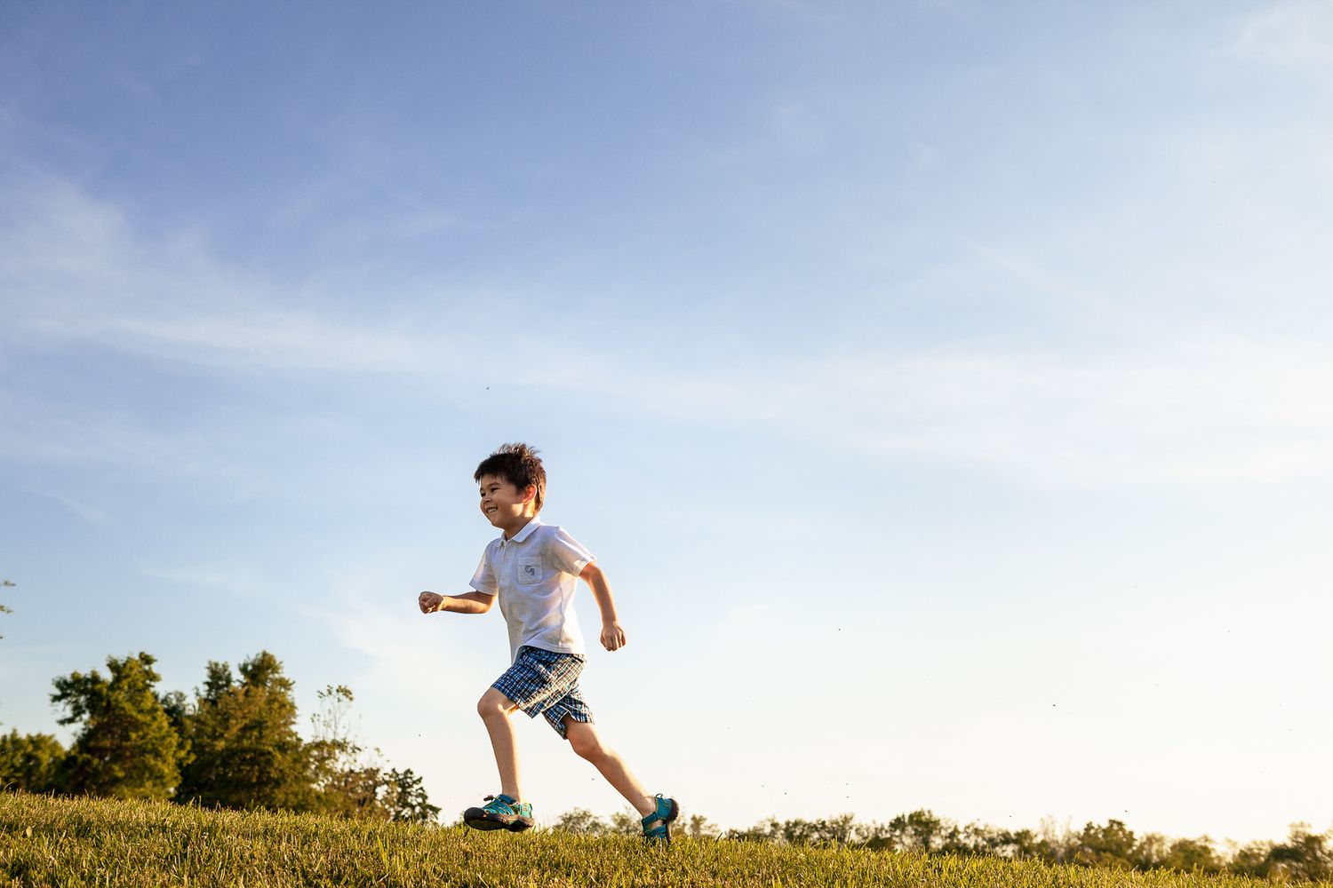 A young boy running joyfully across a green grass field under a bright blue sky on a sunny day.