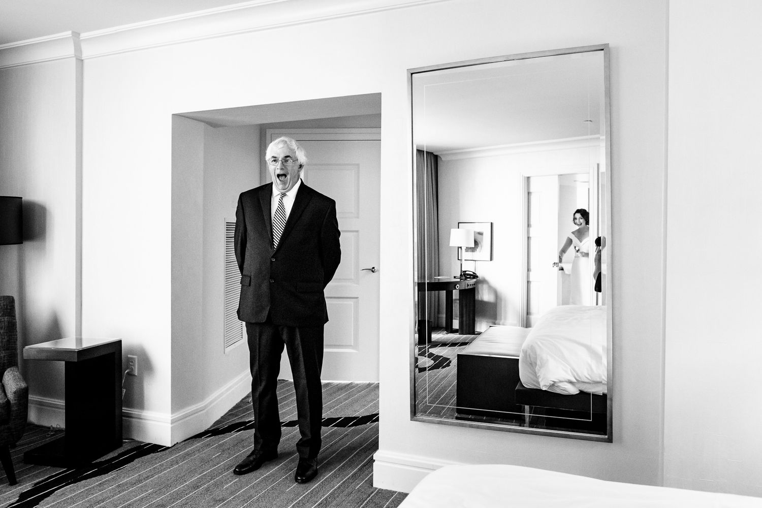 Black and white photo of father seeing bride standing near mirror reflecting bride.
