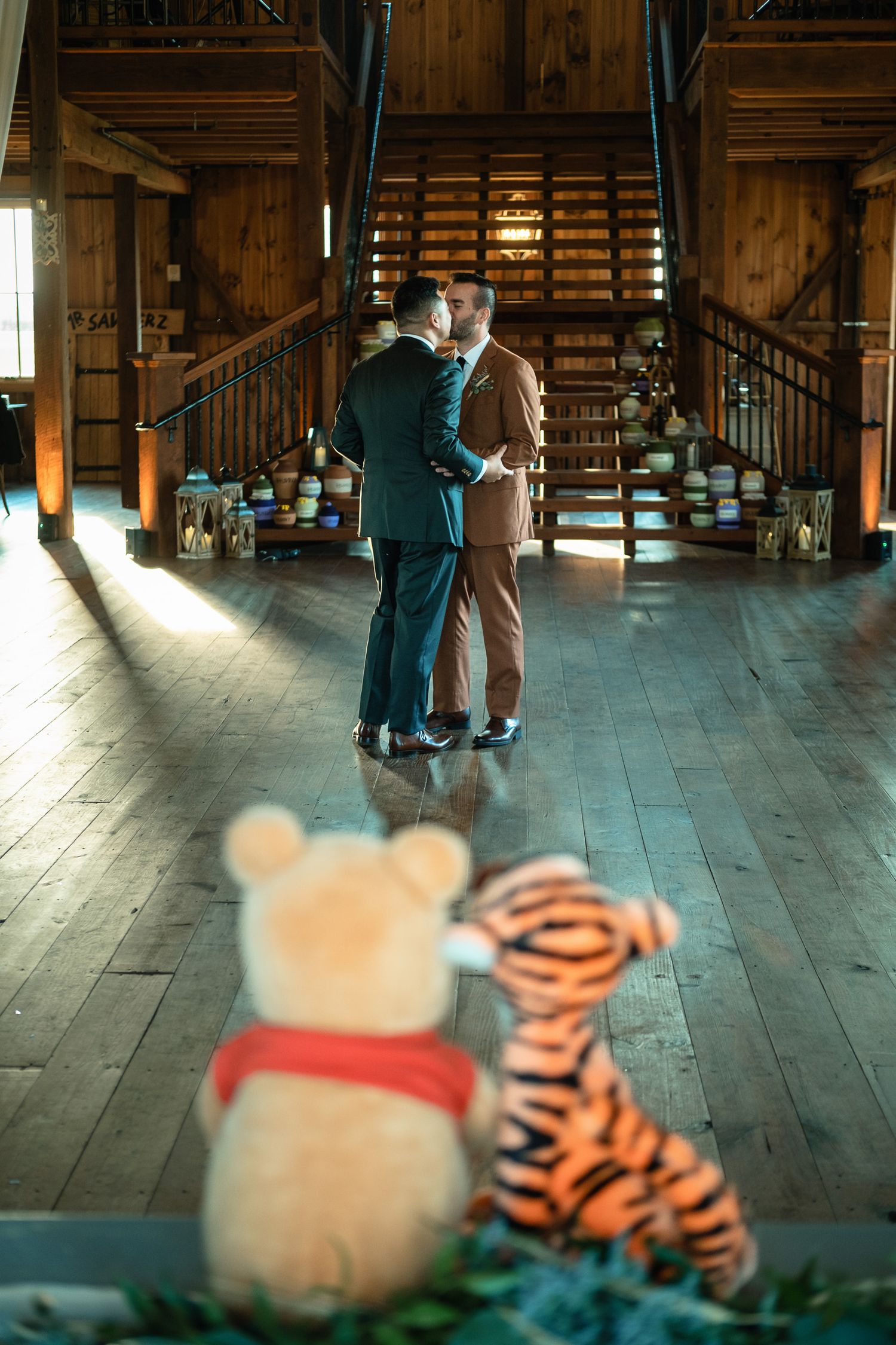 Winnie the Pooh and Tigger stuffed animals watch two grooms dance in barn.