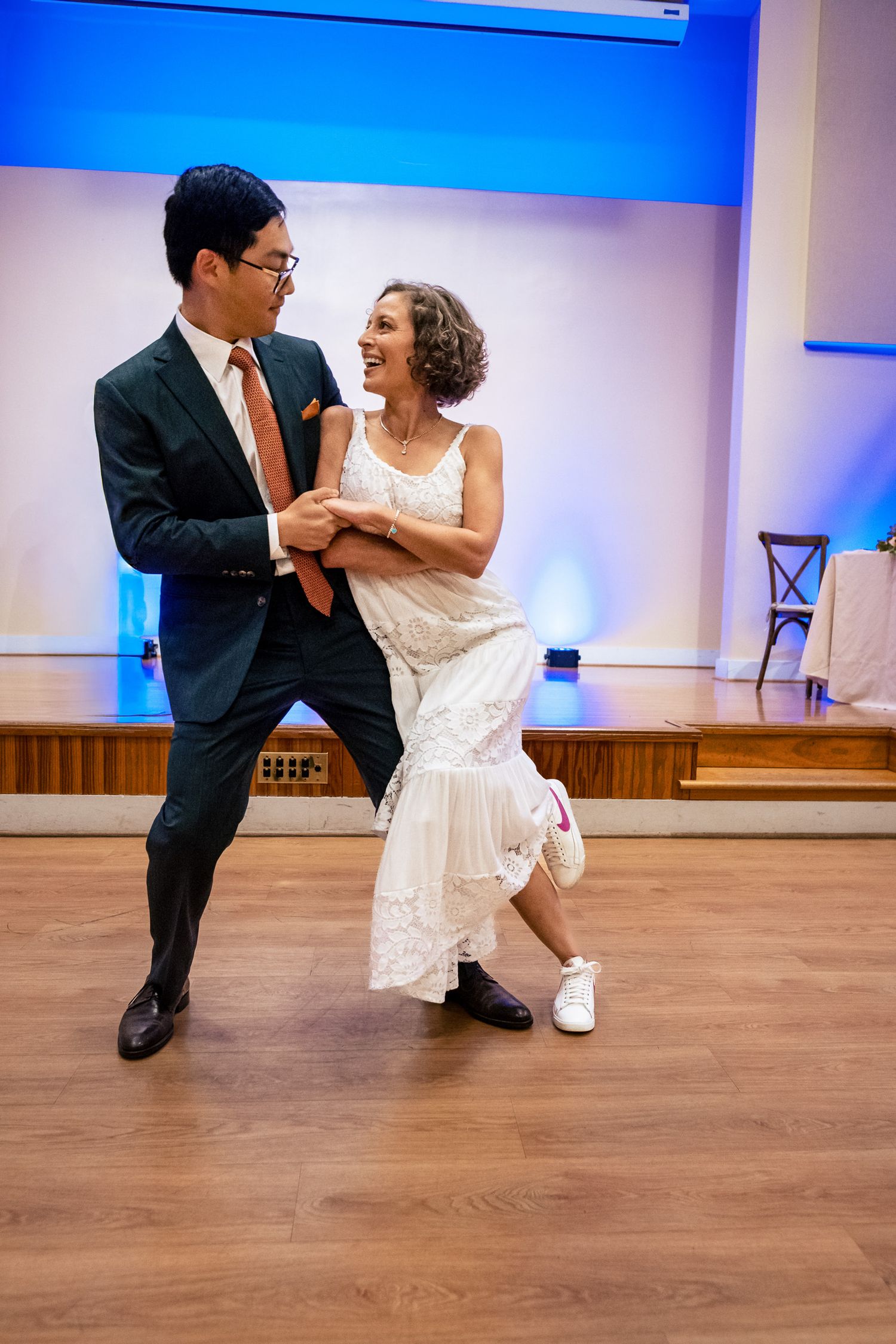 Bride in white lace dress and groom in dark suit dance closely, smiling at each other.