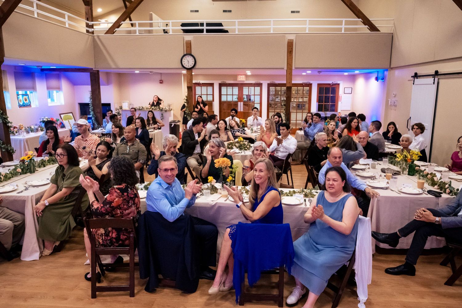 Wedding reception hall filled with guests seated at decorated tables with floral centerpieces.
