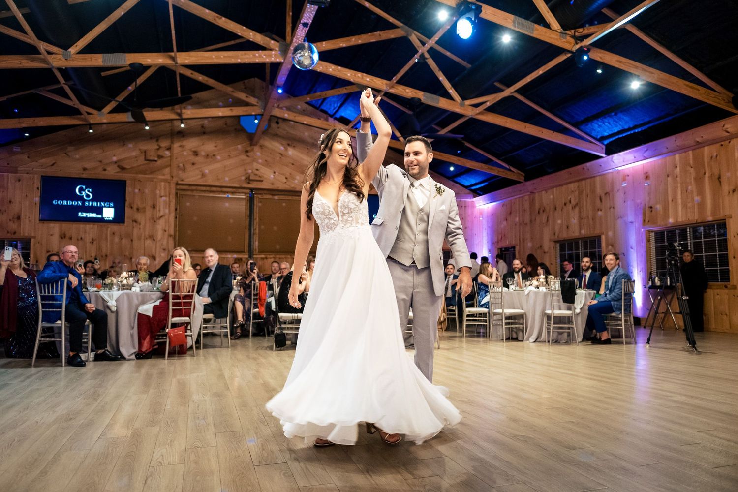 Couple dancing joyfully at wedding reception in elegant barn with blue lighting.