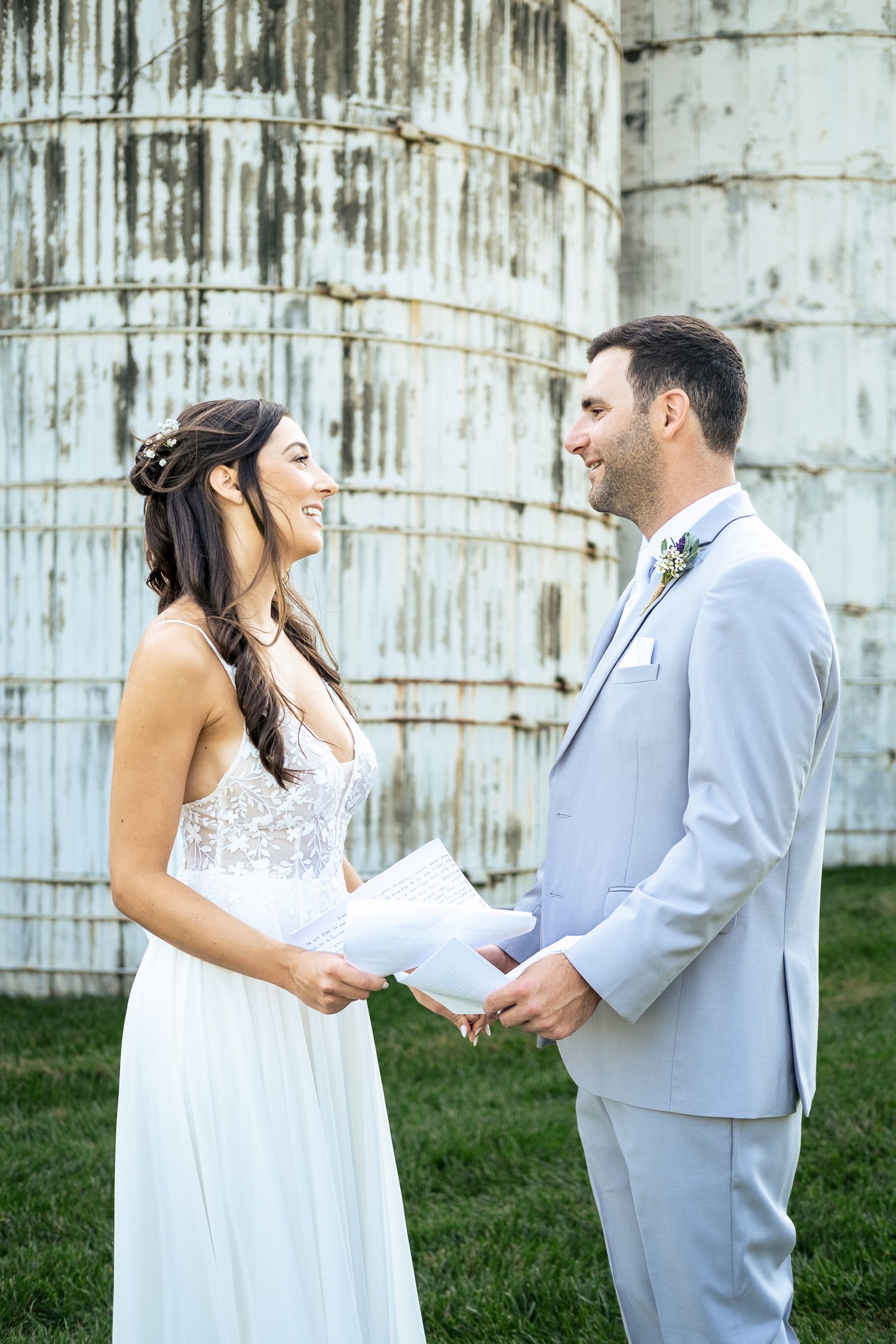 Bride and groom exchange vows outdoors near a rustic grain silo on their wedding day.