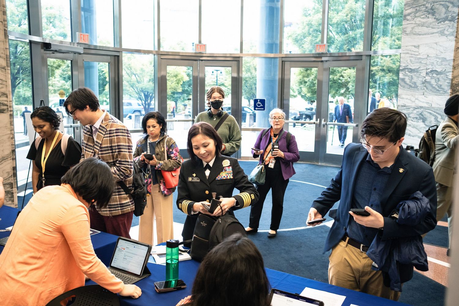 People networking at a registration table in a modern building lobby during a professional conference event.