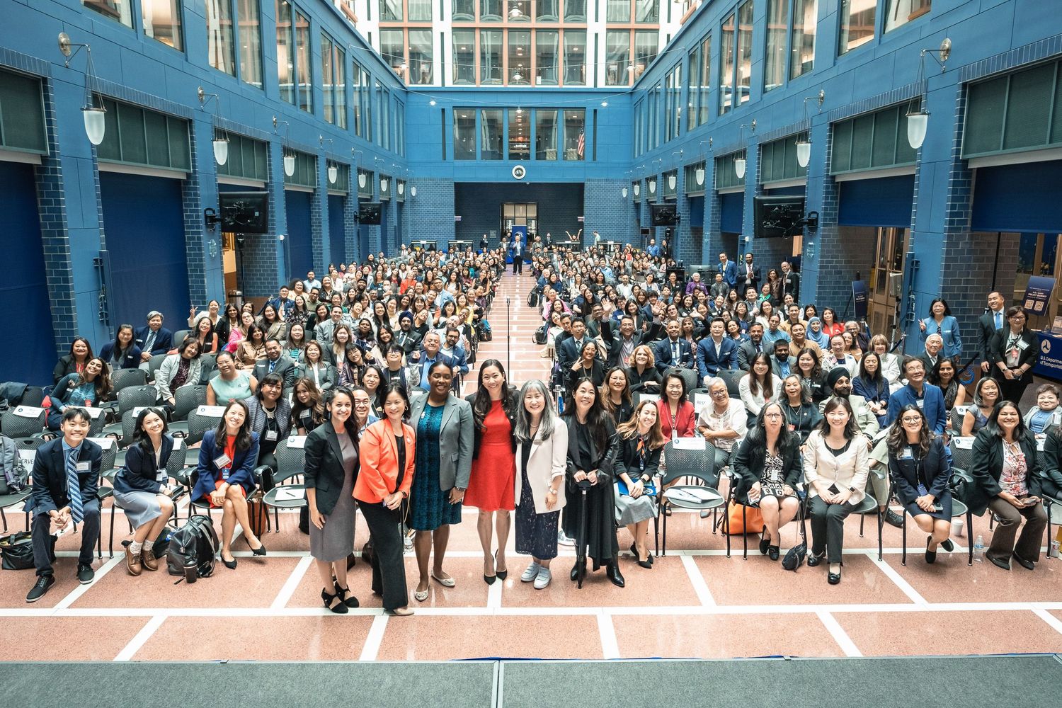 Large group photo of diverse attendees at AA NHPI White House Policy Summit in blue atrium venue.