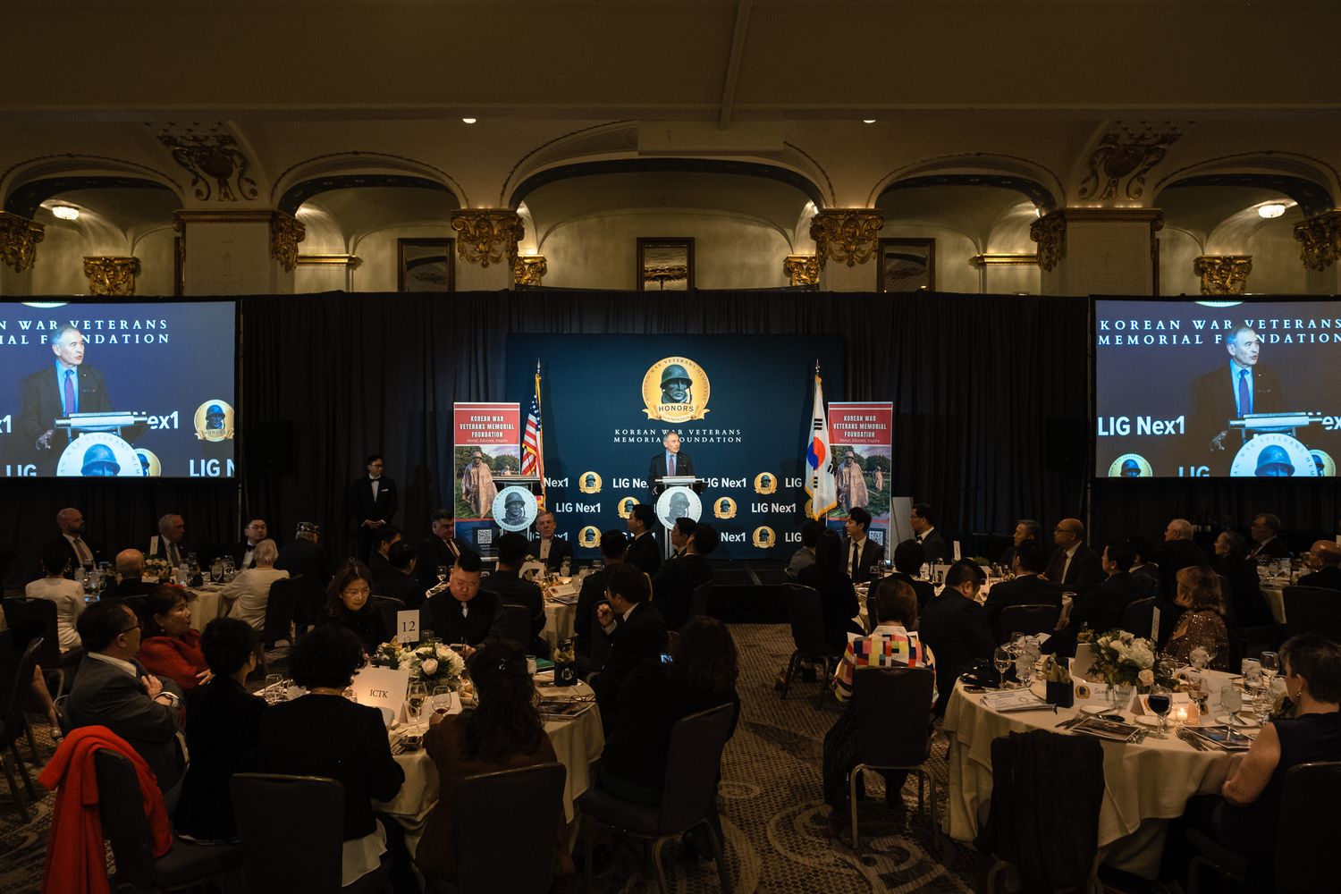 Korean War Literary Foundation awards banquet in grand ballroom with attendees at round tables and large screens displaying event branding.
