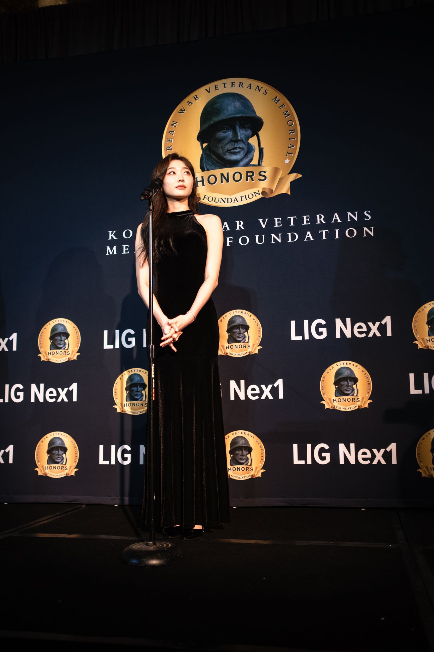 Woman in black gown speaks at microphone at Korean War Veterans Memorial Foundation Honors ceremony.