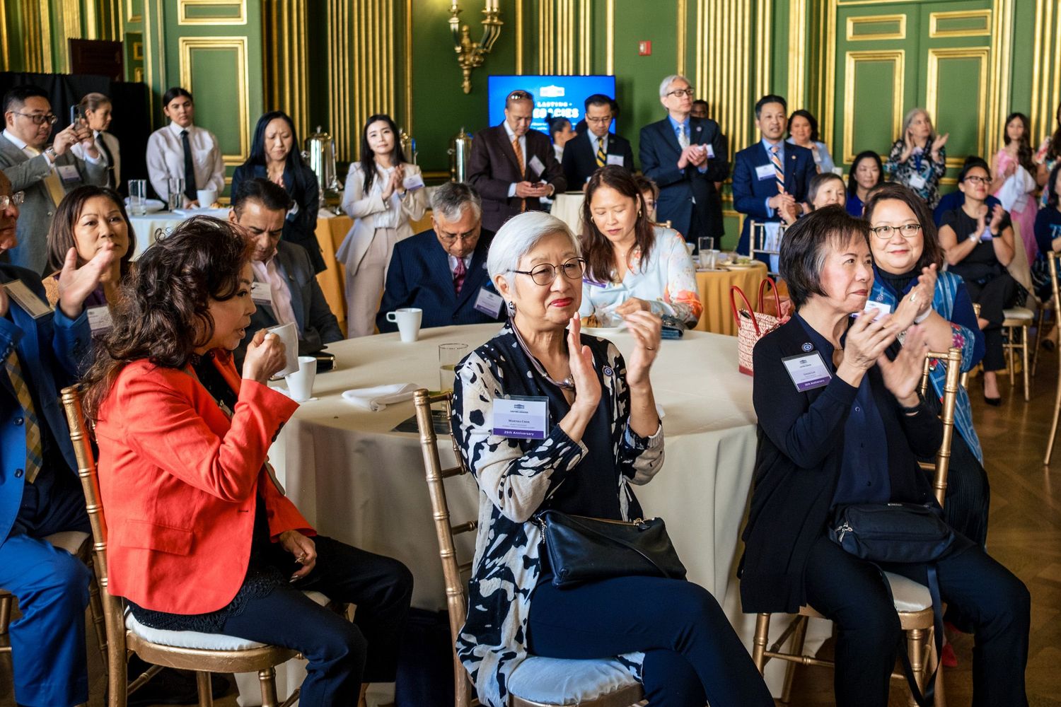 Diverse group of professionals applauding at a formal networking event in an elegant green-walled banquet hall.