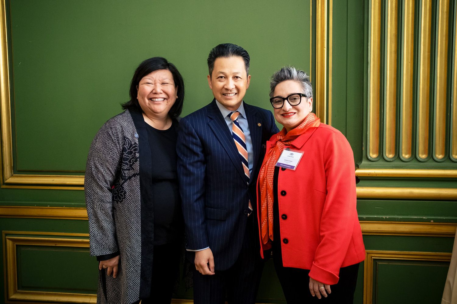 Three professionals posing together at a formal event in front of a green wall.