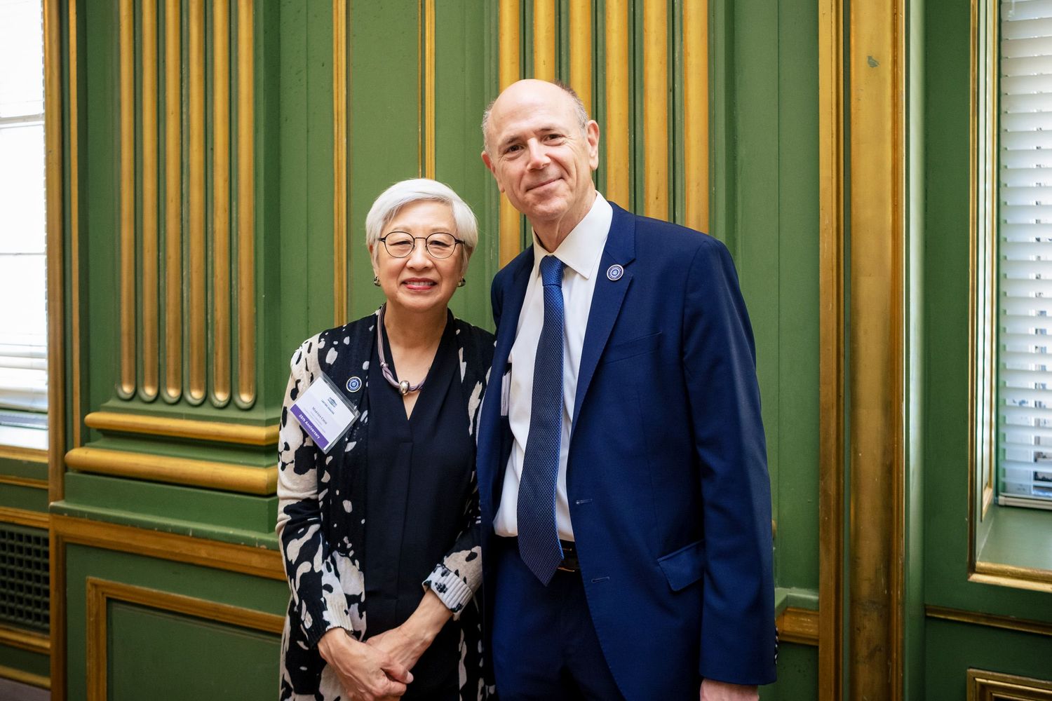 A woman and man in formal attire posing together in an elegant green-paneled room.