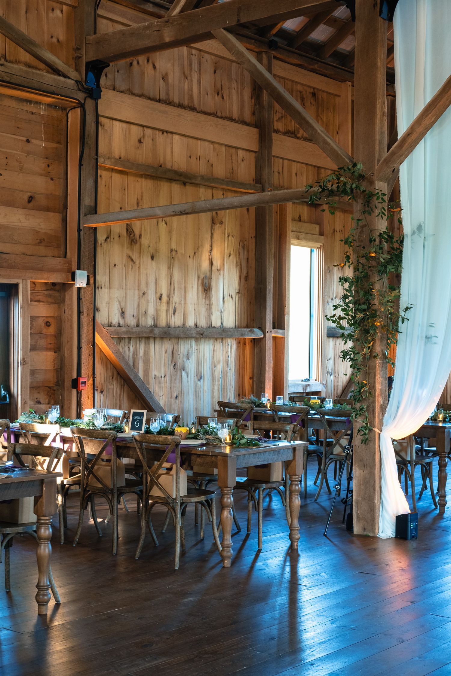 Rustic barn wedding reception interior with wooden walls, long dining tables, and greenery decor.