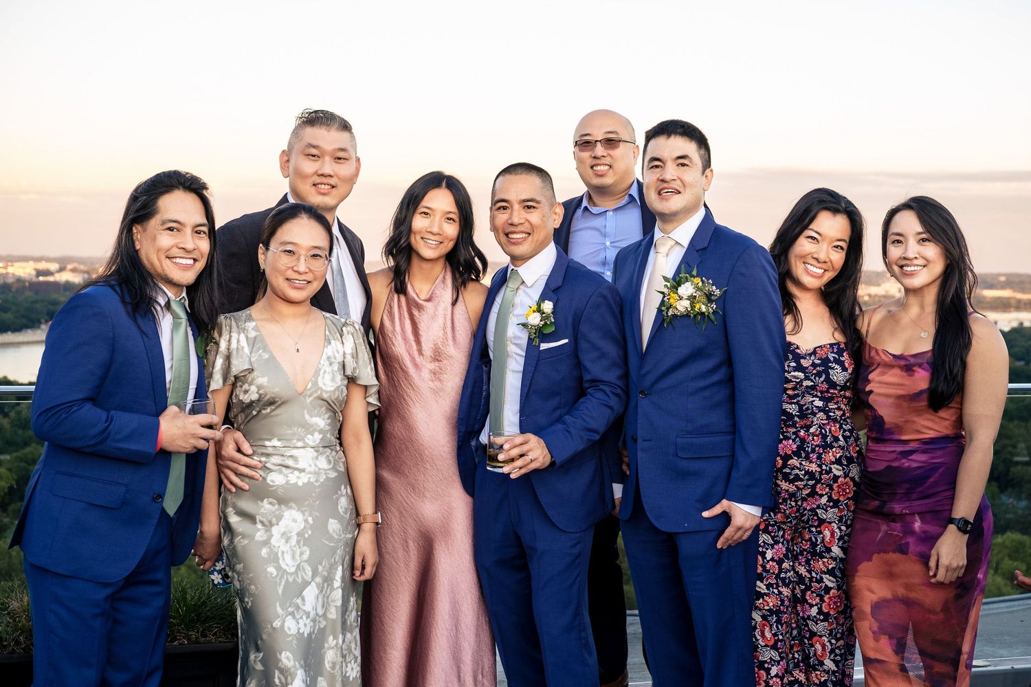 Group of nine wedding guests posing together at sunset rooftop reception.