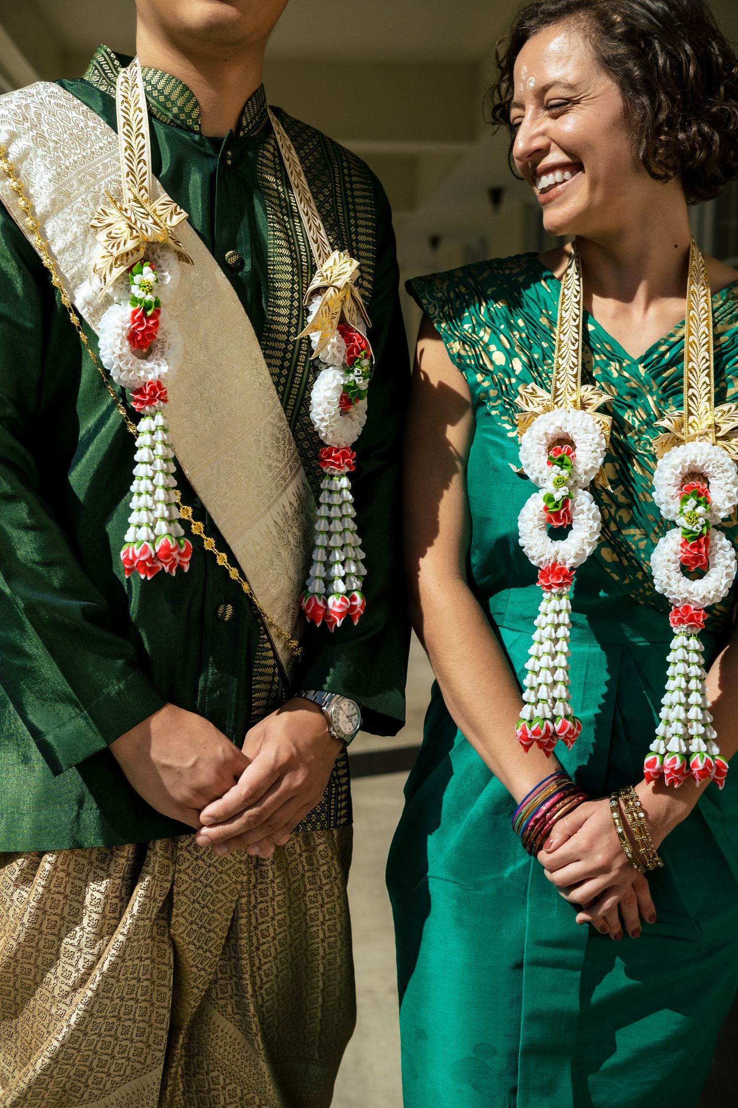 Close-up of couple in traditional Thai green wedding attire with ornate floral garlands.