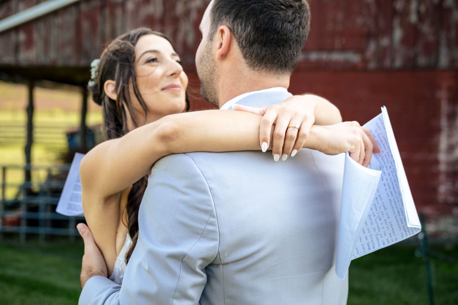 Bride and groom share a tender embrace outdoors with a red barn in the background.