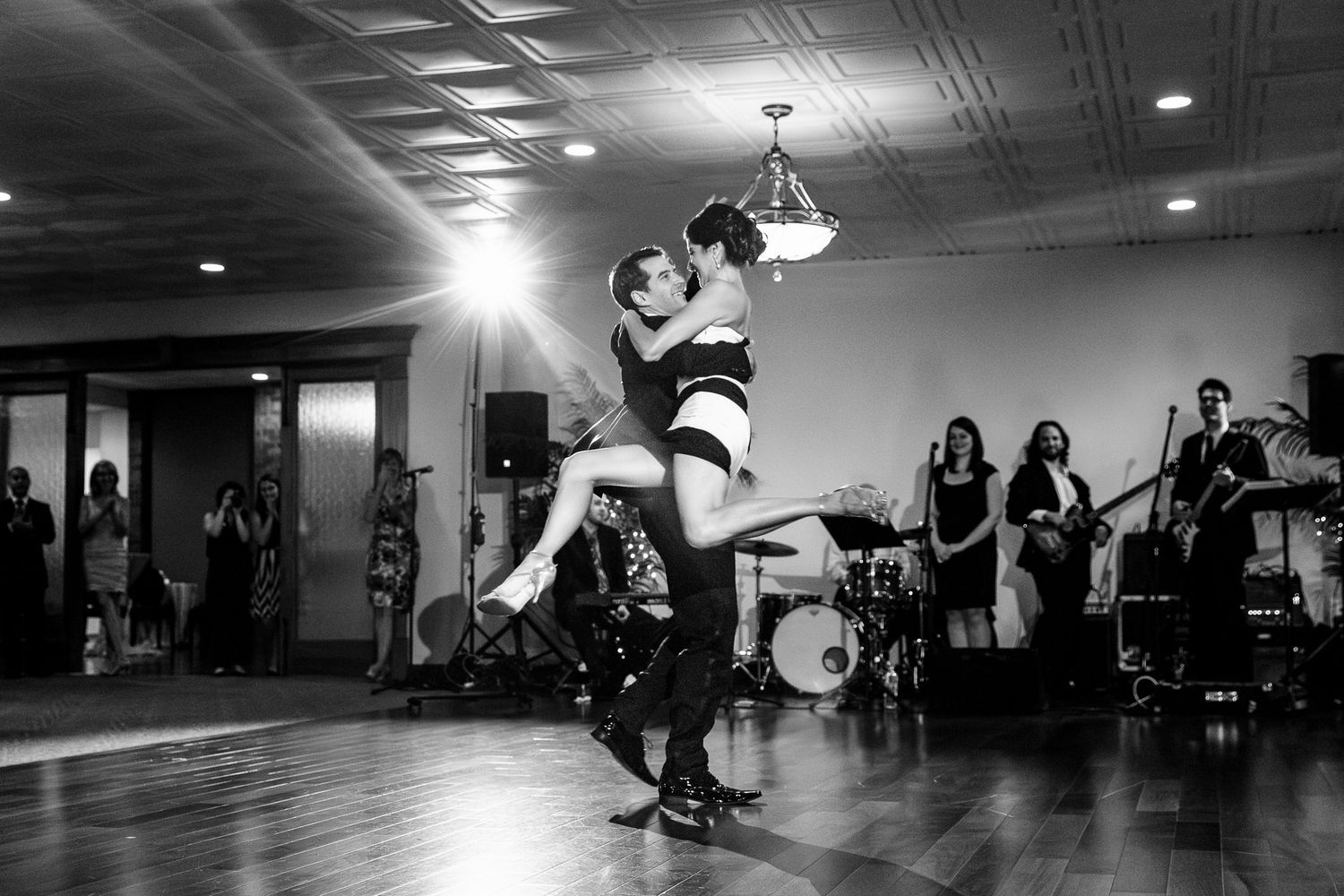 Groom lifts bride in dramatic first dance move while live band performs at wedding reception.