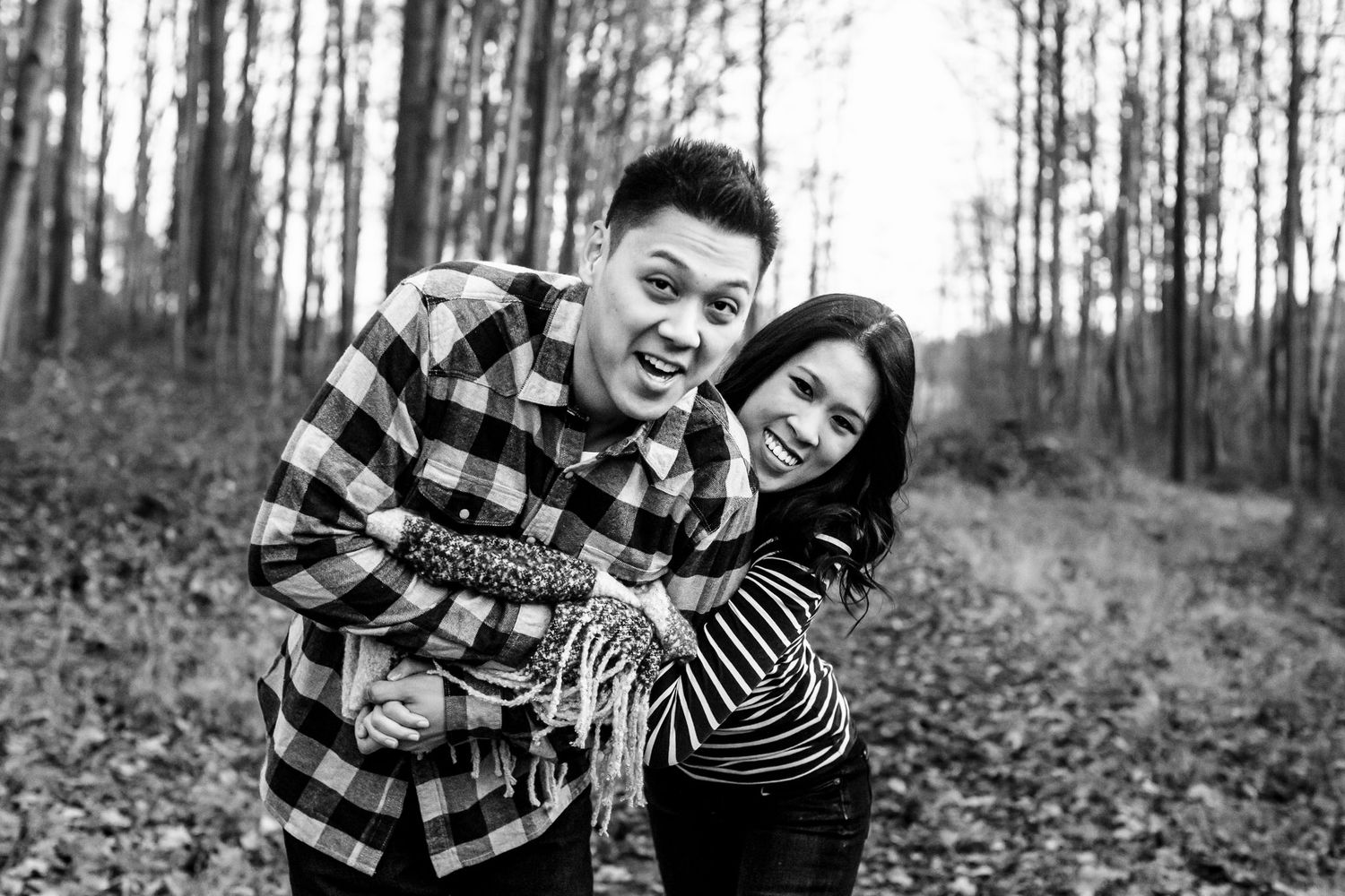 Laughing couple poses playfully together in black and white forest photo.