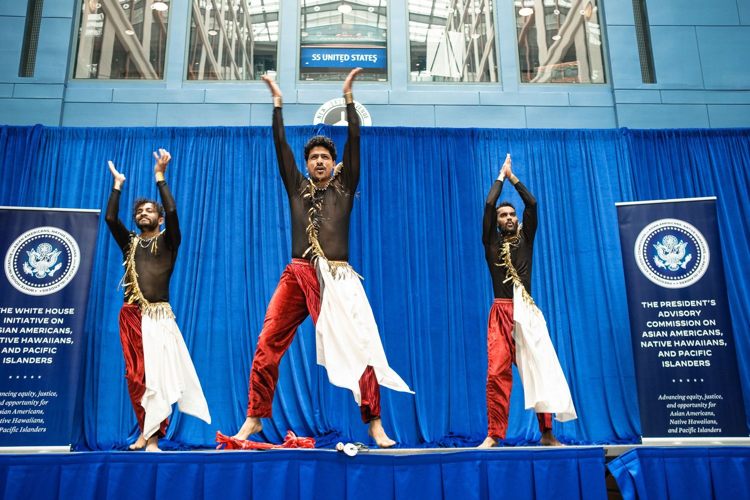Three male dancers perform a traditional South Asian dance on stage at a White House Initiative event.