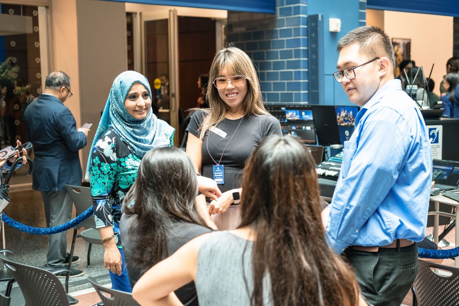 Diverse group of students networking at a university event in a modern venue with blue lighting.