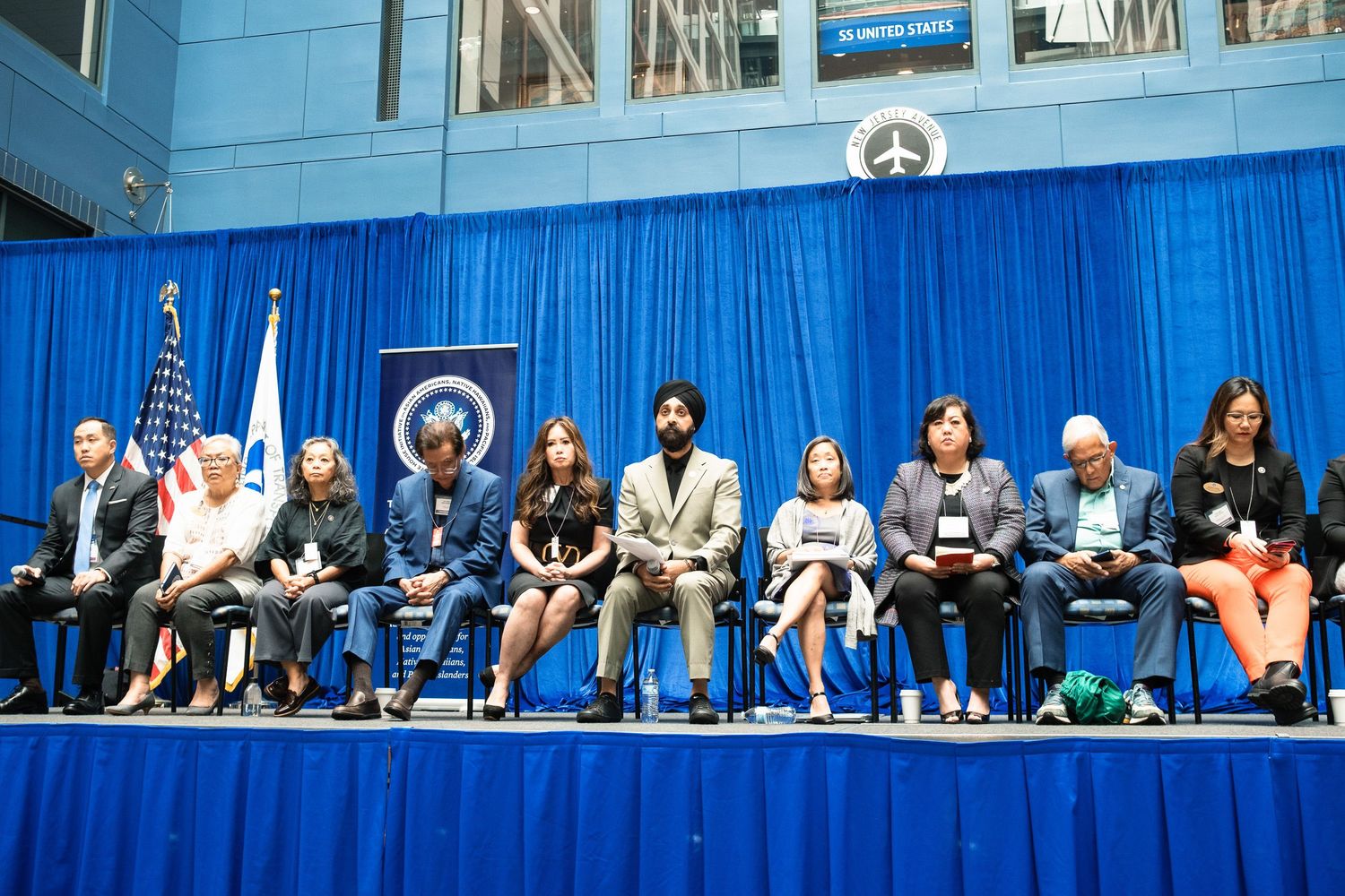 Panel of diverse speakers seated on stage at official government policy summit.