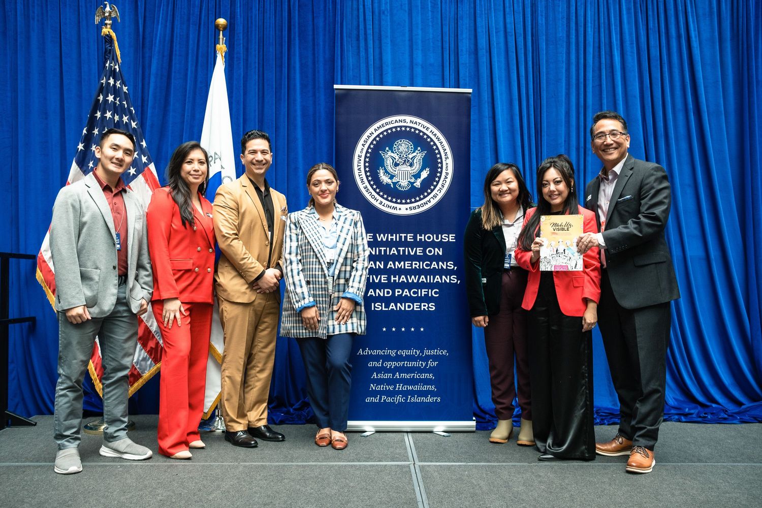 Group of seven people posing in front of White House Initiative on Asian Americans banner at formal event.