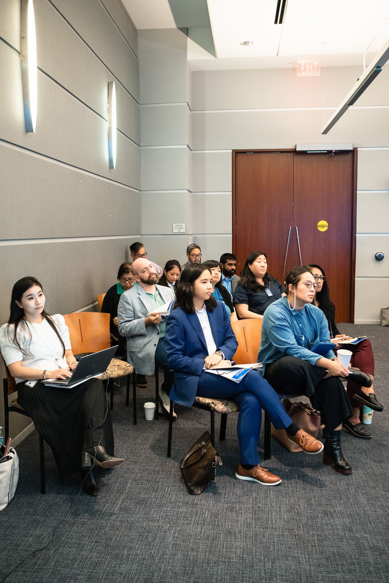 Diverse group of professionals seated in a modern conference room, attentively listening during a business seminar or presentation.