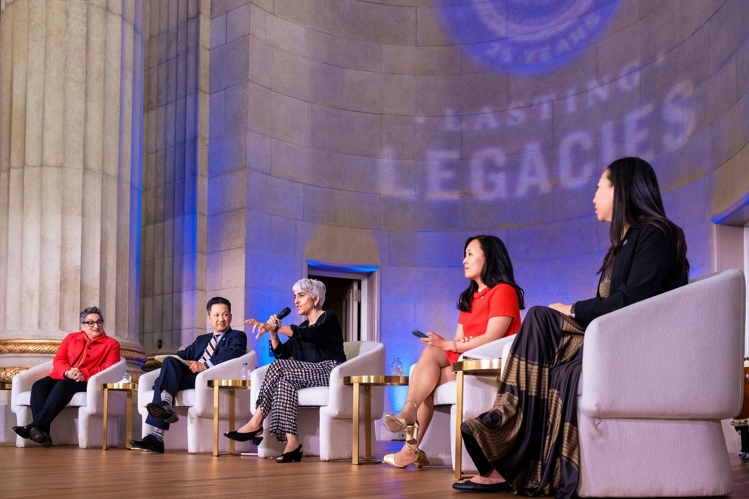 Panel discussion at Lasting Legacies event with four speakers seated on stage in grand hall.