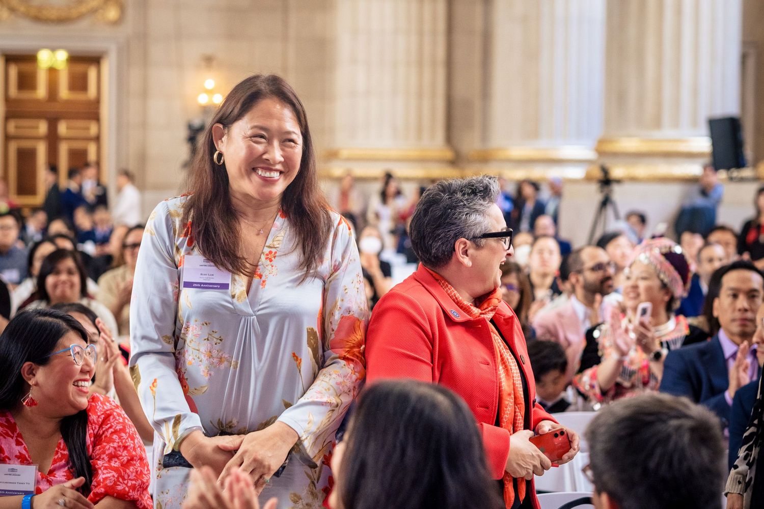 Smiling Asian woman in blue floral dress stands at a festive cultural celebration event indoors.