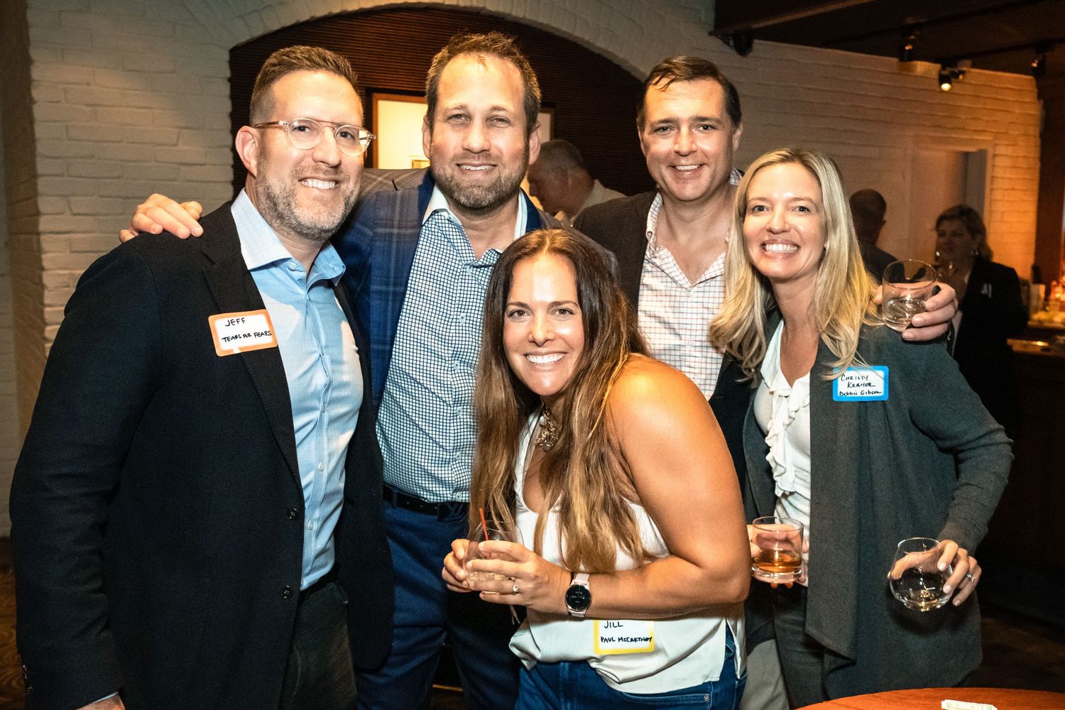 Five professionals smiling and posing together at a corporate networking event wearing name tags.