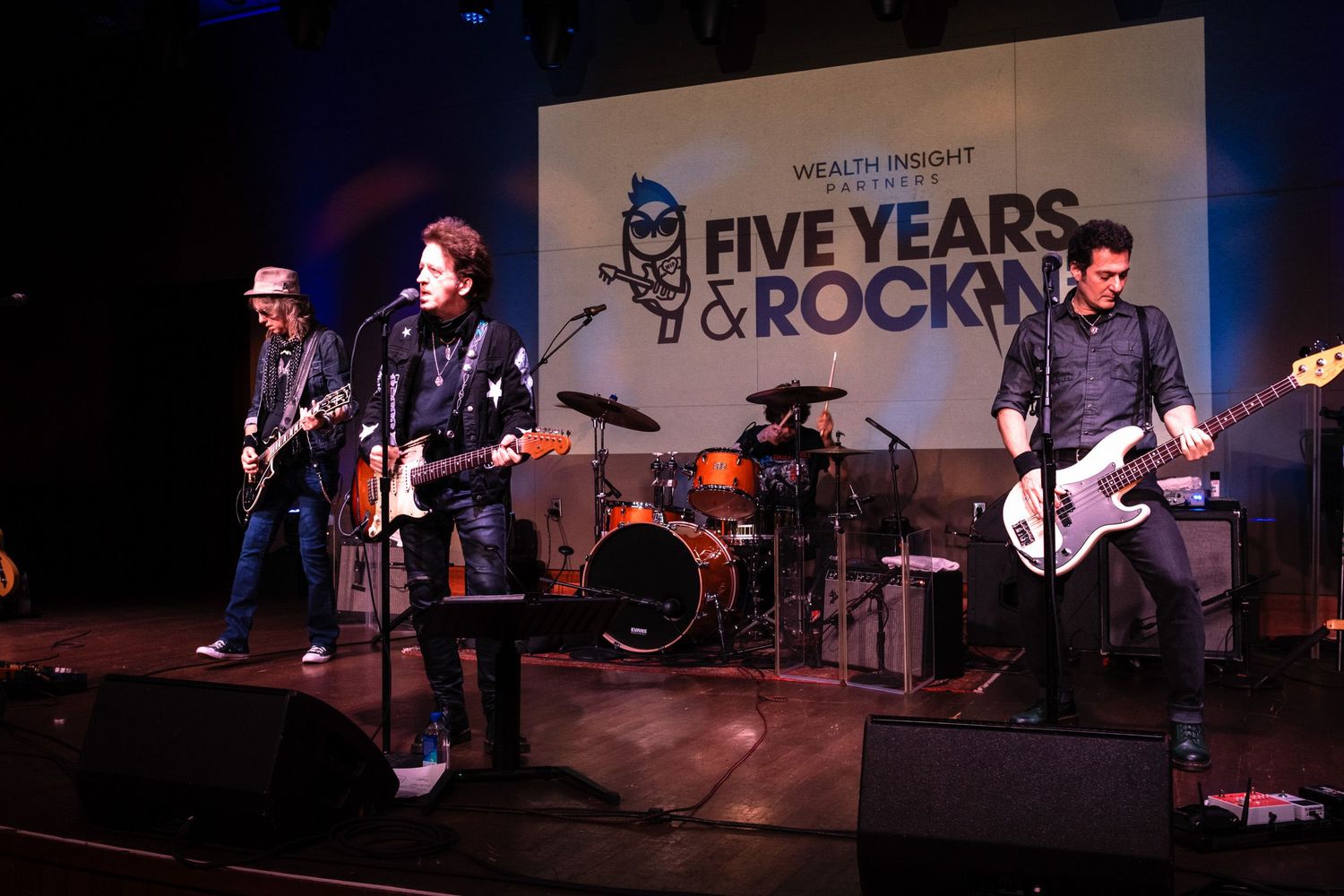 A rock band performs on stage at a Five Years and Rockin anniversary event with colorful stage lighting.