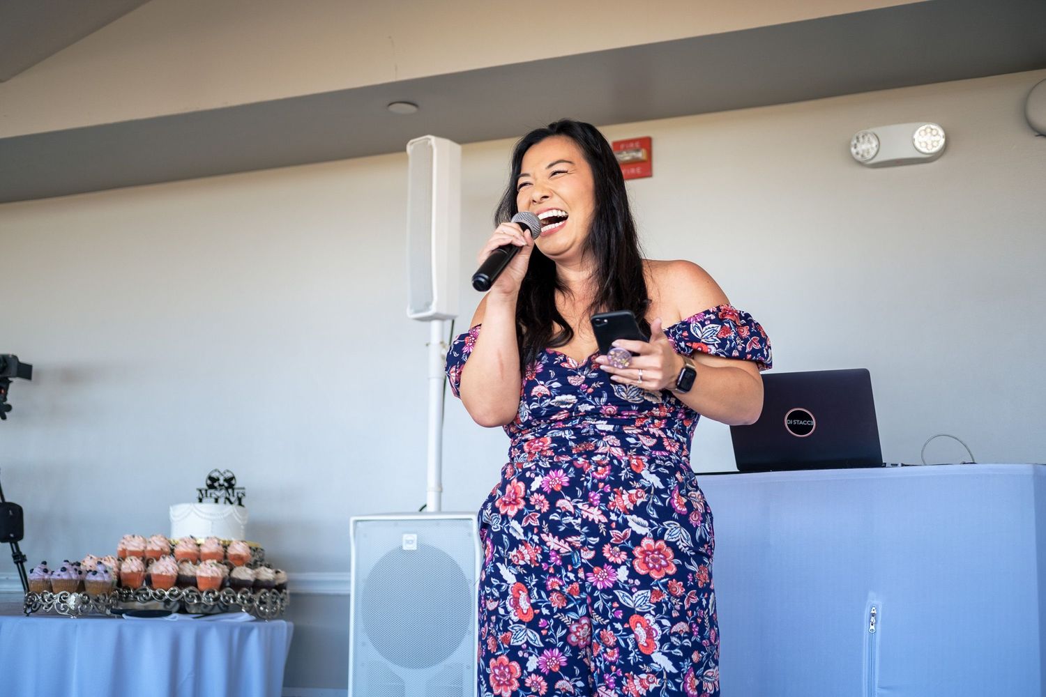 Woman in floral dress singing into microphone at wedding reception event.