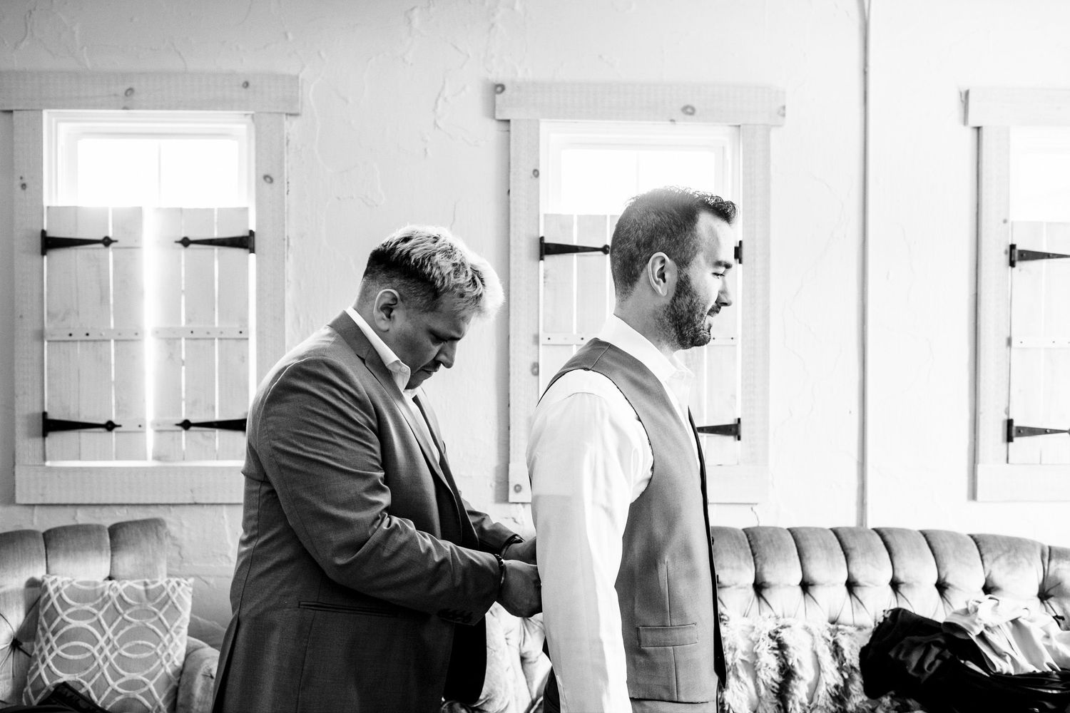 Groomsman helping groom with vest in black and white wedding preparation photo.