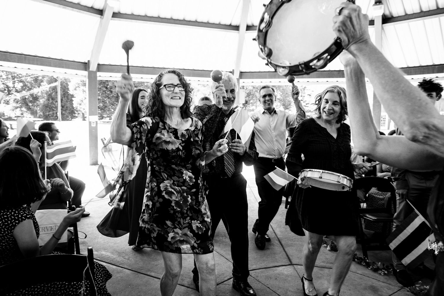 Guests dancing joyfully at an outdoor wedding reception with drums and percussion instruments in black and white photo.