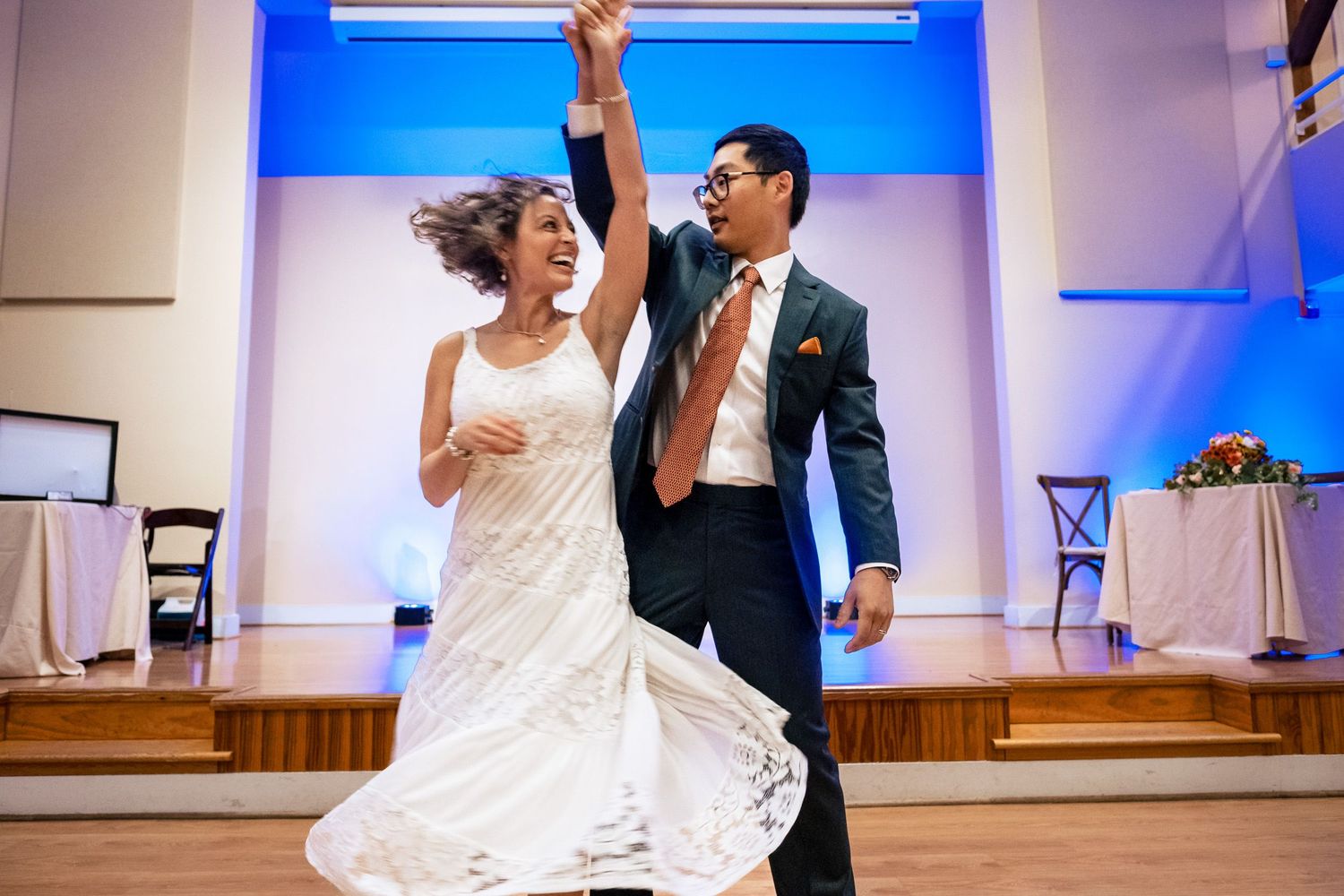 Groom lifts bride's hand as she spins joyfully in white dress during first dance.
