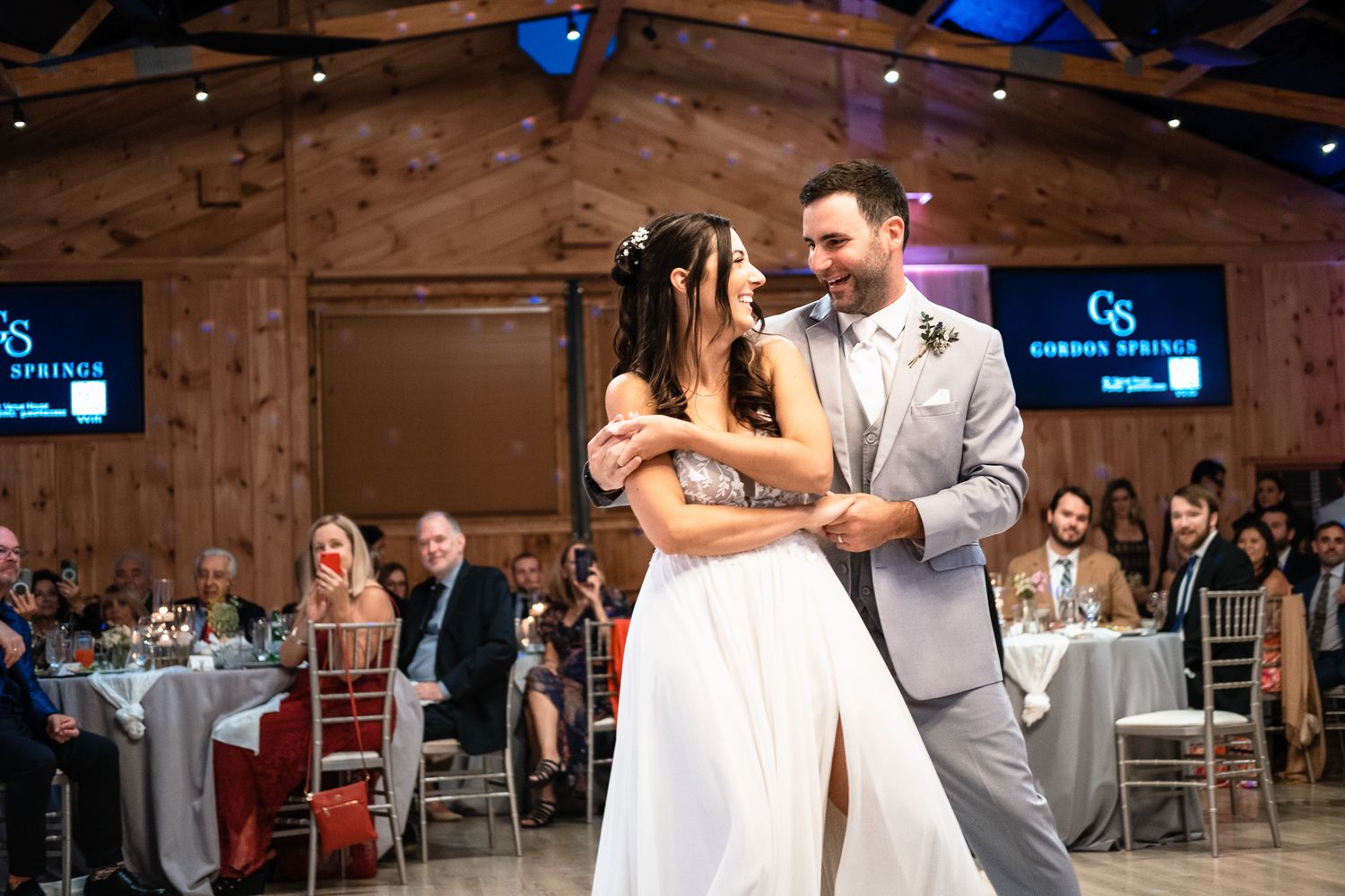 Bride and groom sharing their first dance in a rustic wooden venue with guests watching.