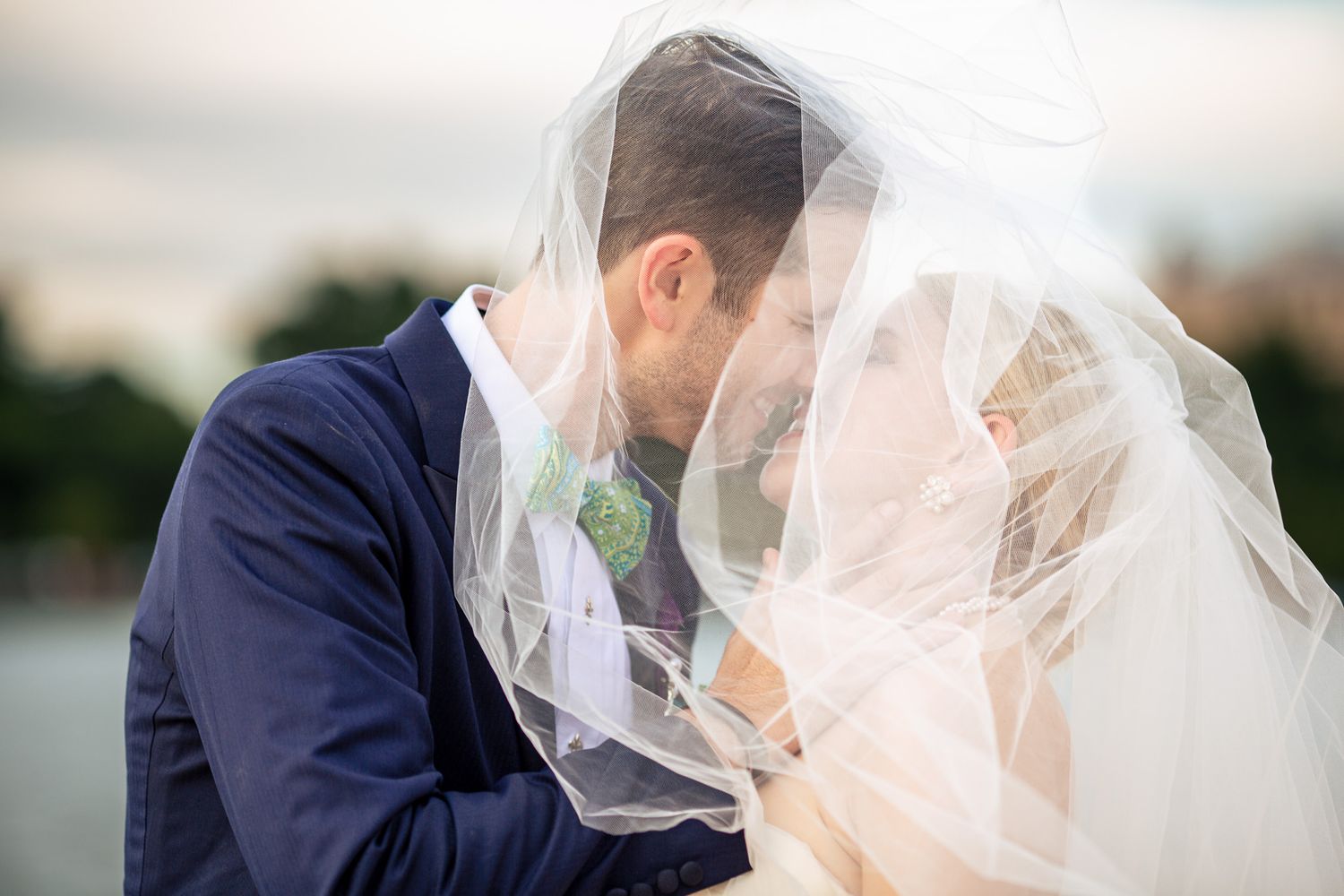 Bride and groom share a romantic kiss hidden beneath the bride's flowing white veil.