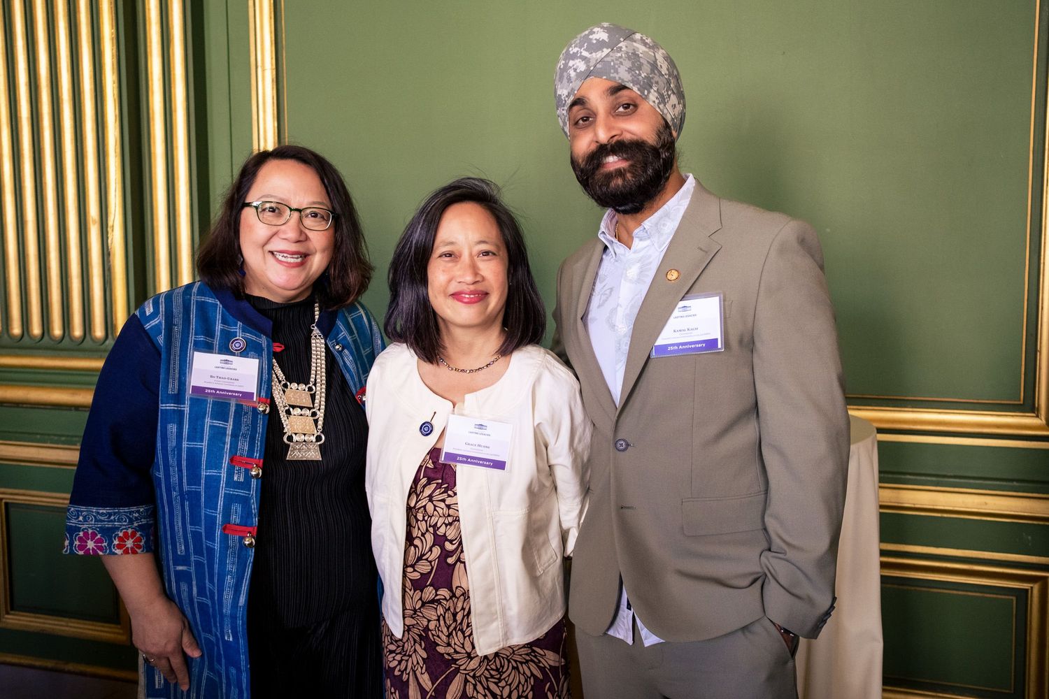 Three professionals smiling together at a formal event, including a man wearing a turban and two women with name badges.