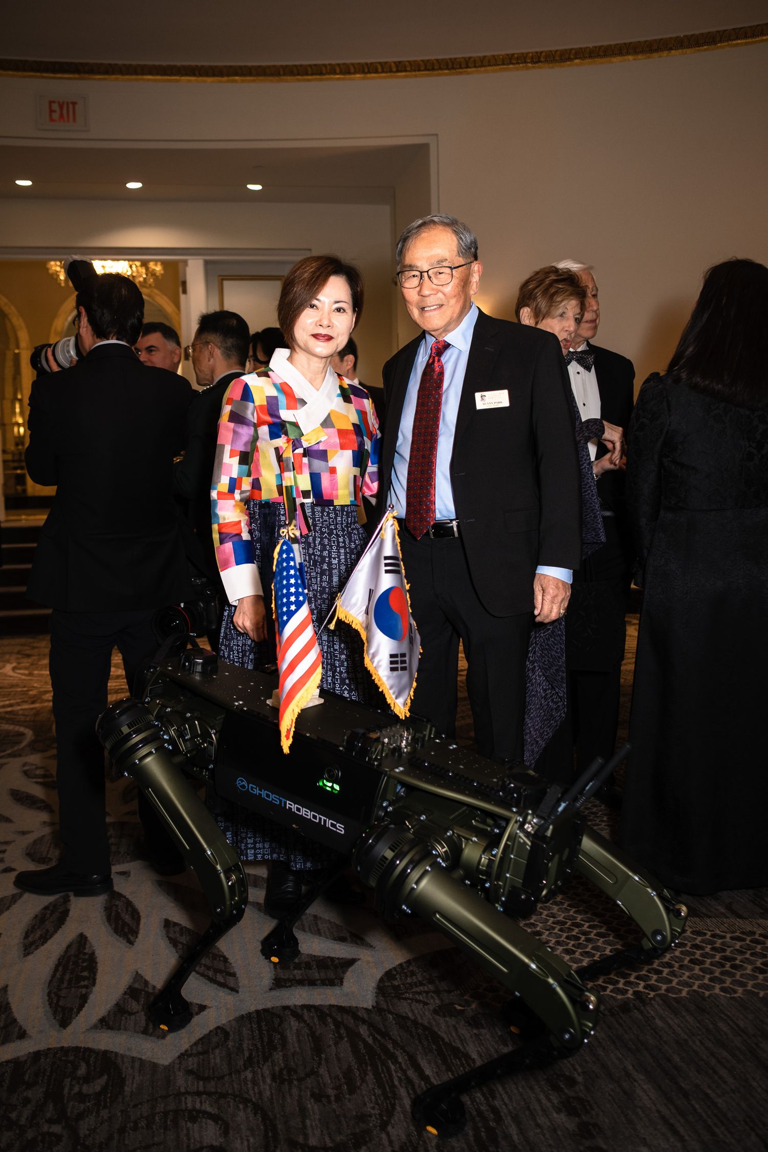 Couple posing with a Boston Dynamics robot dog holding US and South Korean flags at a formal event.