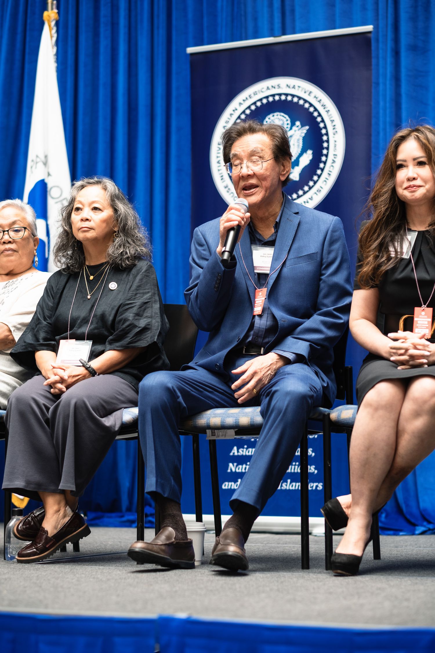 Panel discussion at Asian American Native Hawaiian Pacific Islander event with speakers seated before a presidential seal banner.