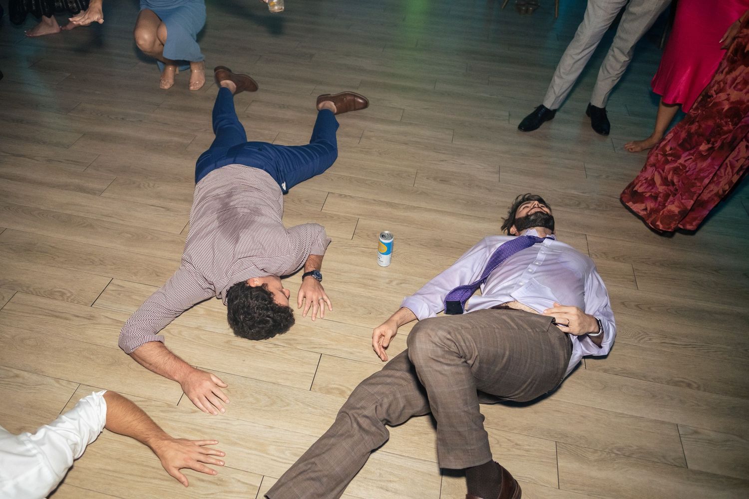 Two wedding guests lying on the dance floor laughing during a lively wedding reception party.