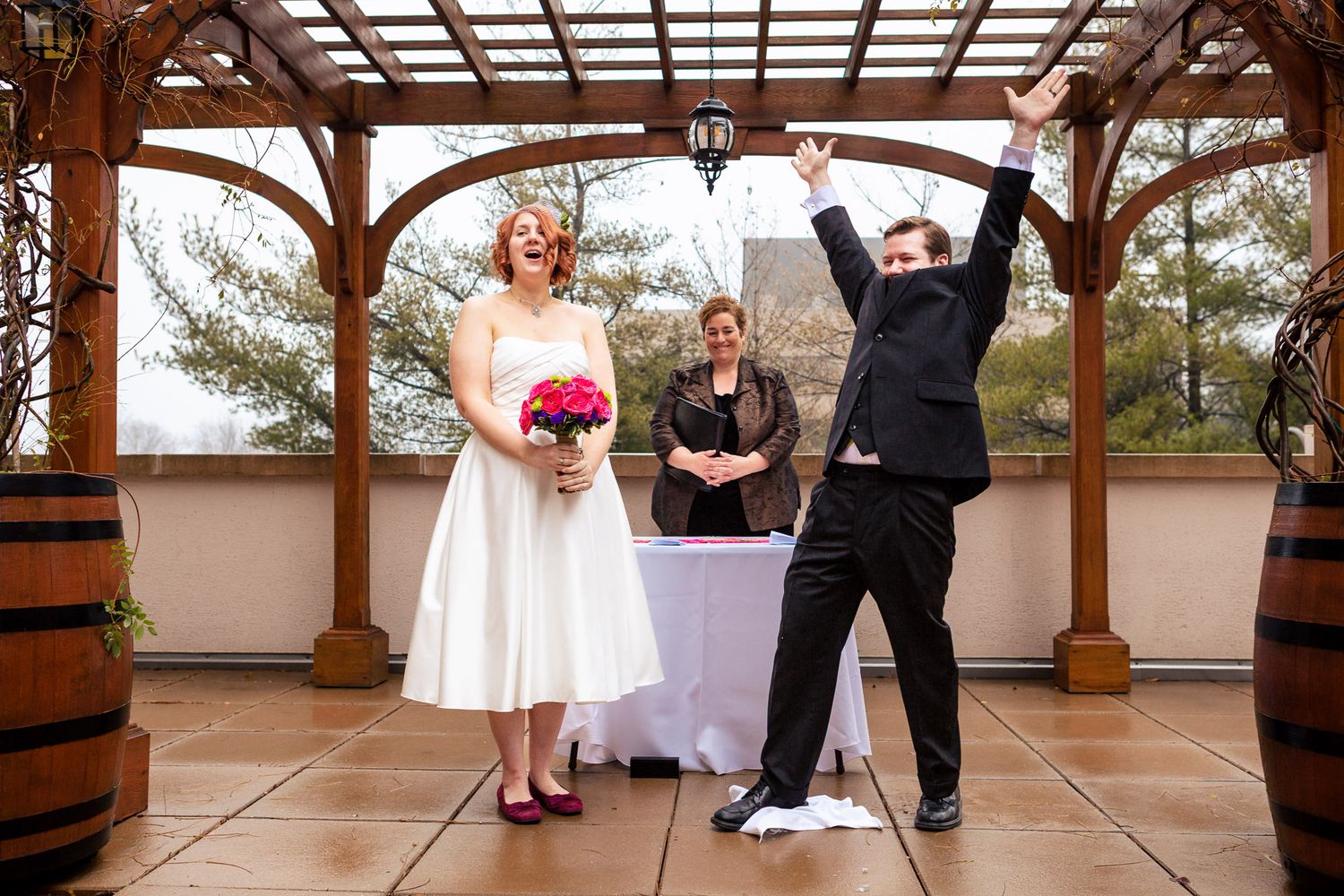 Bride and groom celebrating joyfully with officiant on an outdoor terrace after ceremony.